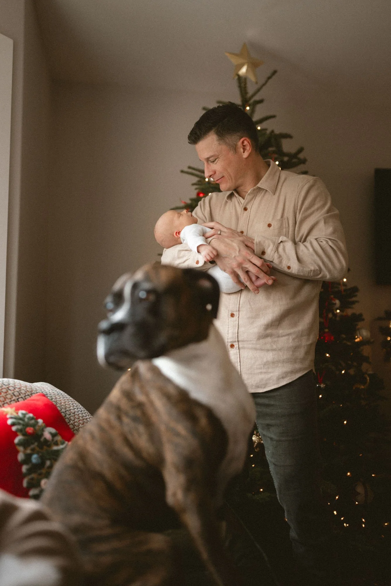 A father holds his newborn baby near a Christmas tree during a cozy in-home newborn photography session in Seattle.