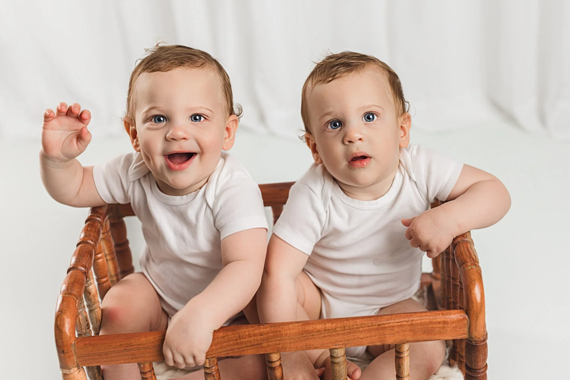 Smiling twin babies sitting side by side during a Seattle baby milestone photography session in a studio.