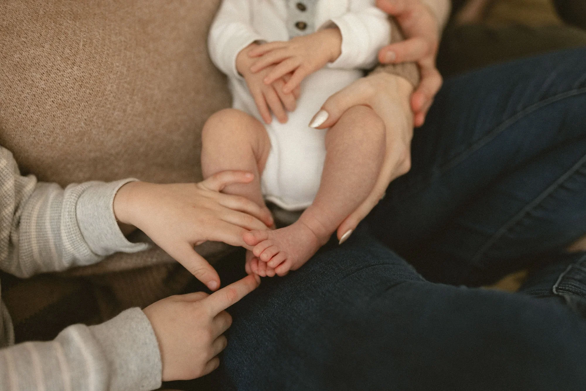 Close-up of a newborn’s tiny toes being gently touched by an older sibling during an in-home newborn family photography session in the Bellevue and Redmond area by Atsumi Sullivan Photography.