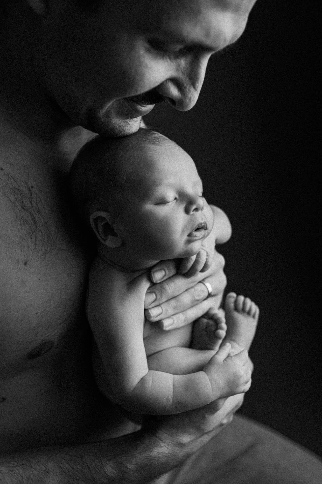 Father gently holding his newborn against his chest, capturing the tenderness and calm of those early days in an intimate, minimalist portrait.