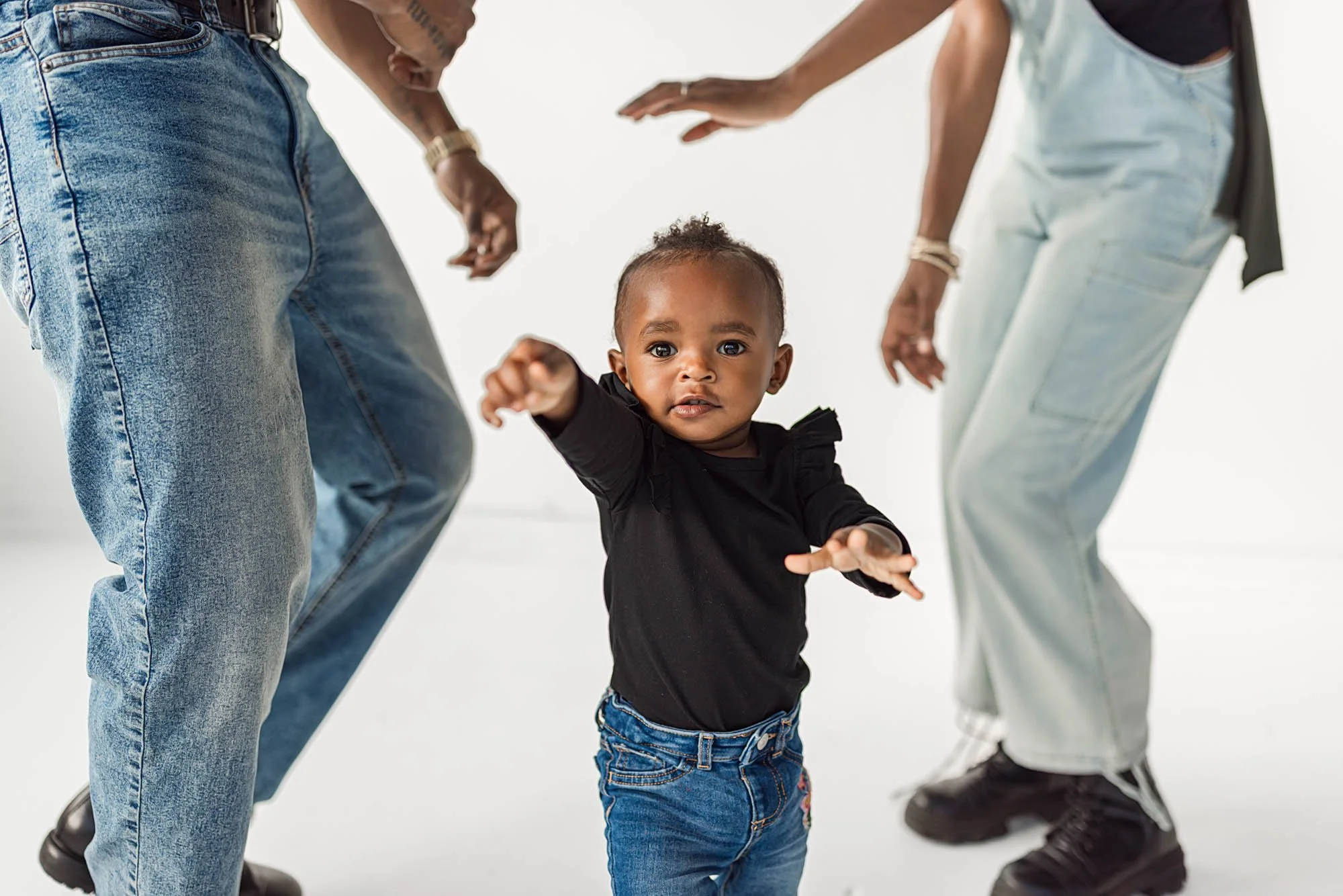 Baby reaching forward while standing between parents during a natural light studio family photography session in Seattle near Uwajimaya.