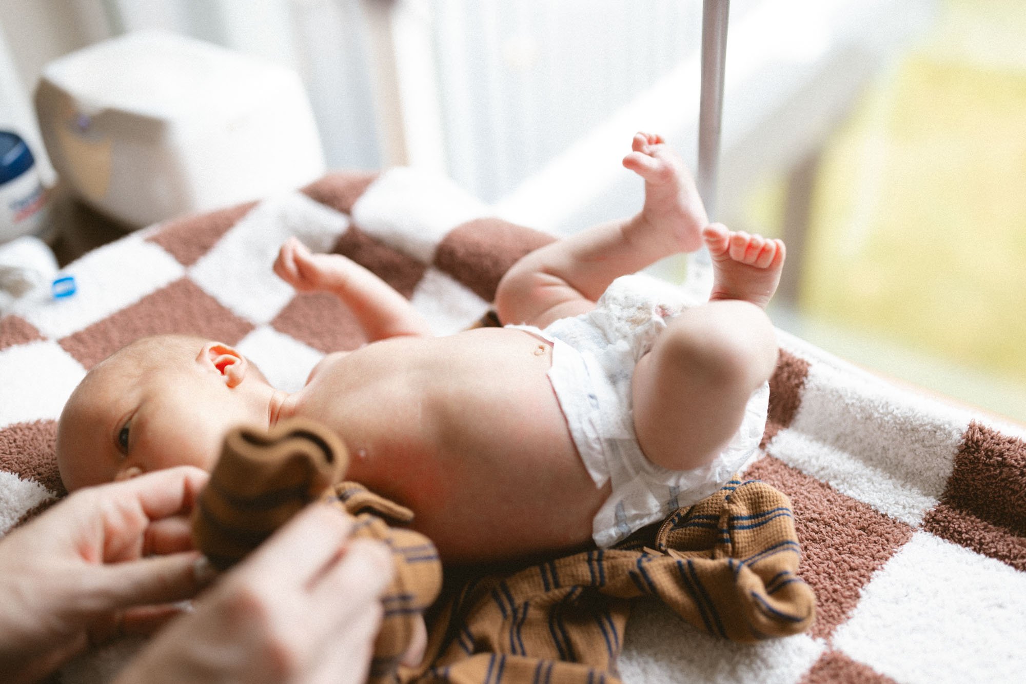 A newborn baby lying on a soft blanket during a gentle in-home diaper change, photographed in natural window light in Seattle.