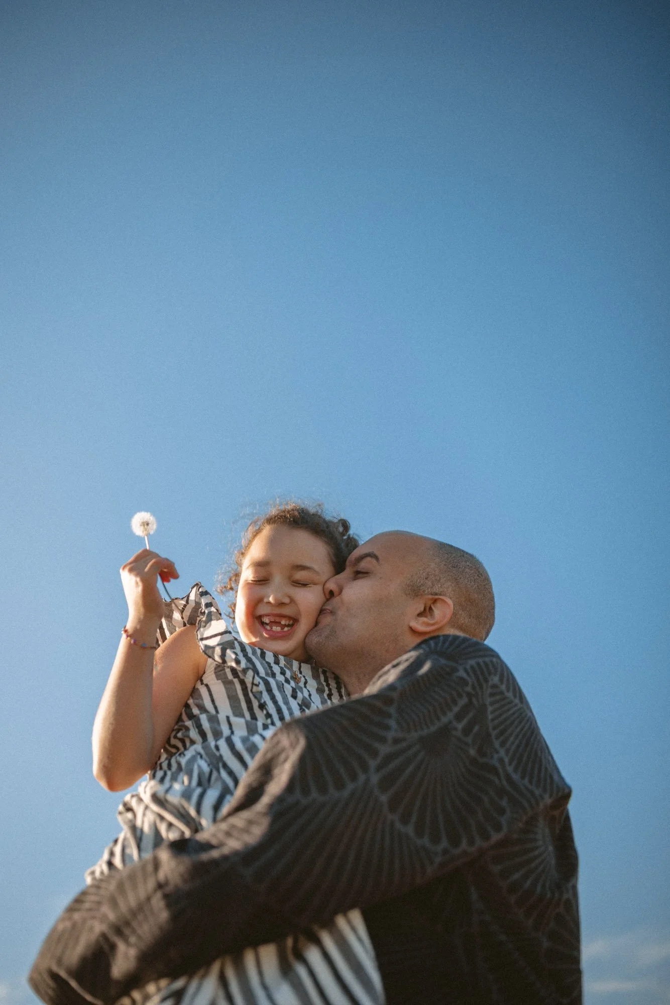 Father holding and kissing his daughter during a playful outdoor family photography session in Seattle.