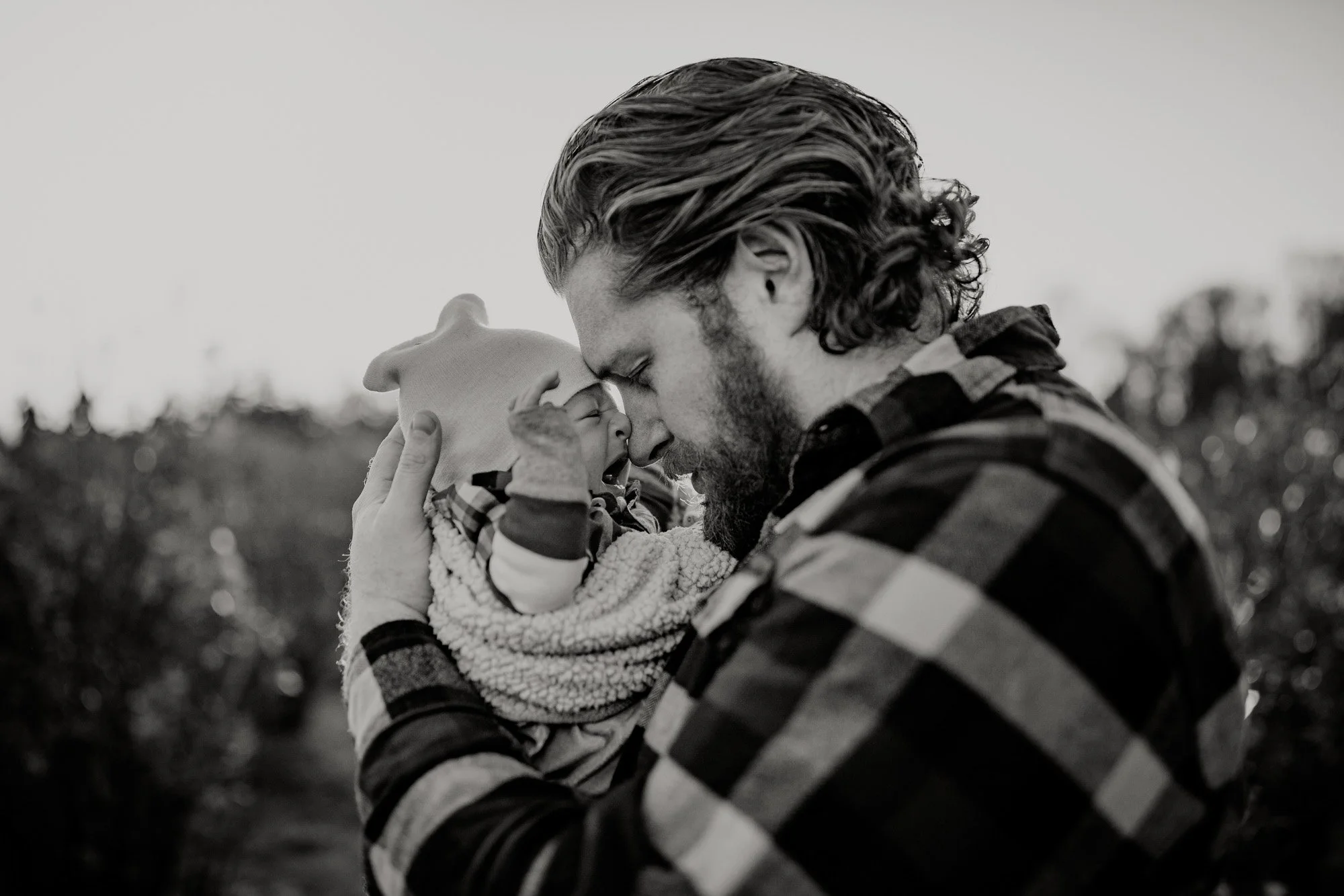 Father gently holding and touching noses with his baby during an outdoor session in Lake Tapps, captured by a Lake Tapps family photographer