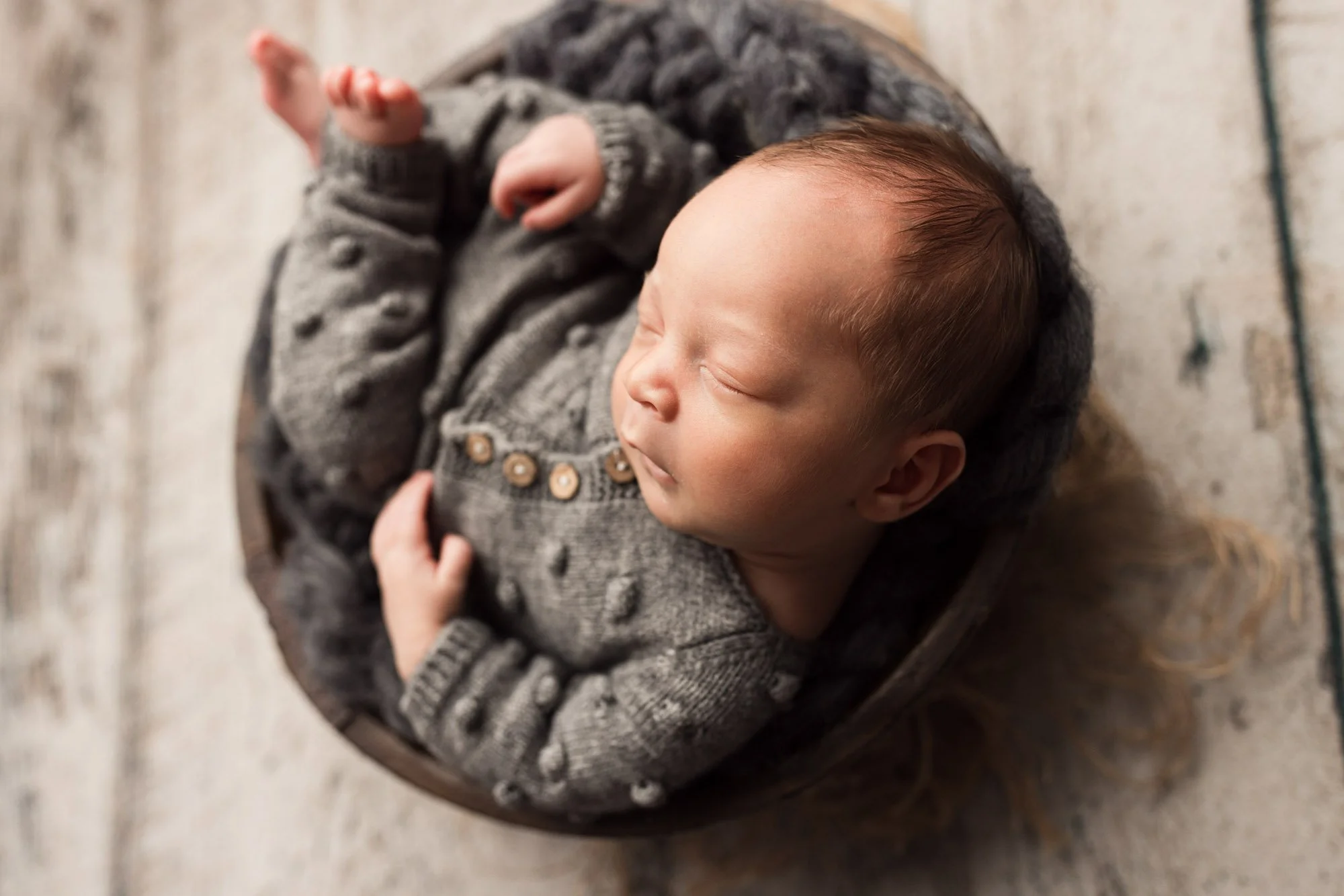 Close-up of a sleeping newborn baby in a textured gray outfit and basket