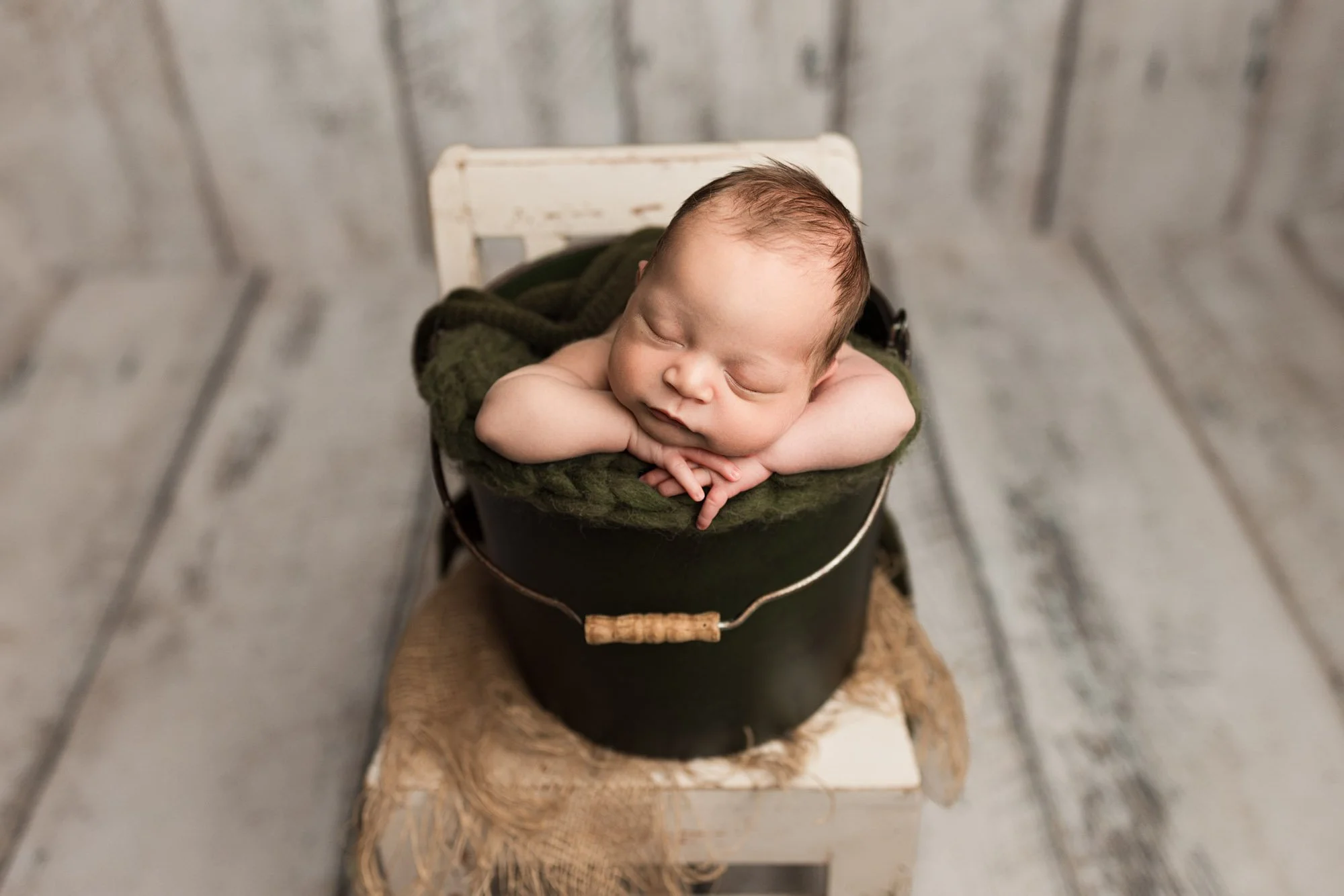 Sleeping newborn baby posed safely in a small bucket with a green knitted layer