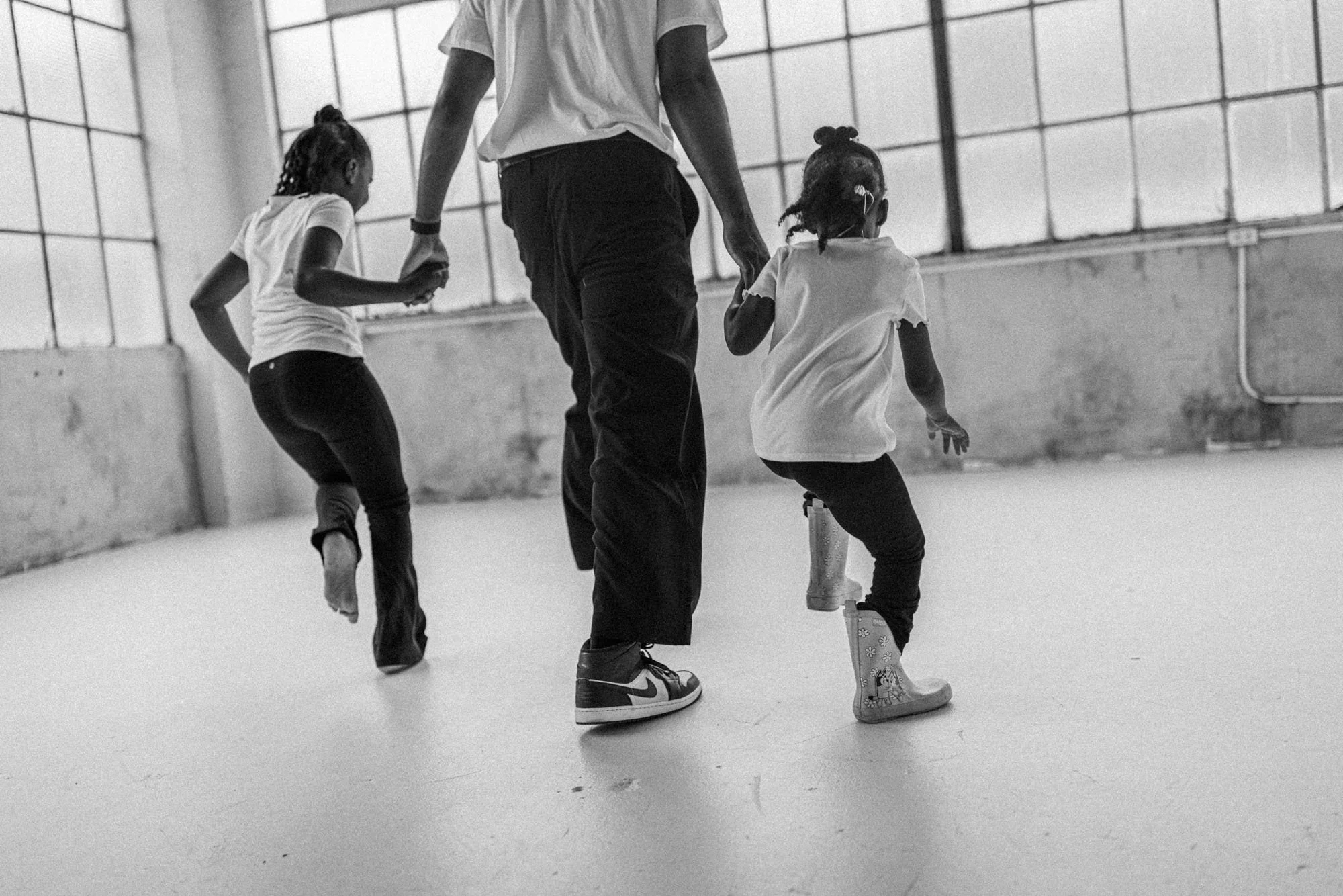 Children walking hand-in-hand with a parent during a candid family session in a bright studio, photographed by a Seattle family photographer. Black and white lifestyle image capturing movement, connection, and authentic childhood moments.