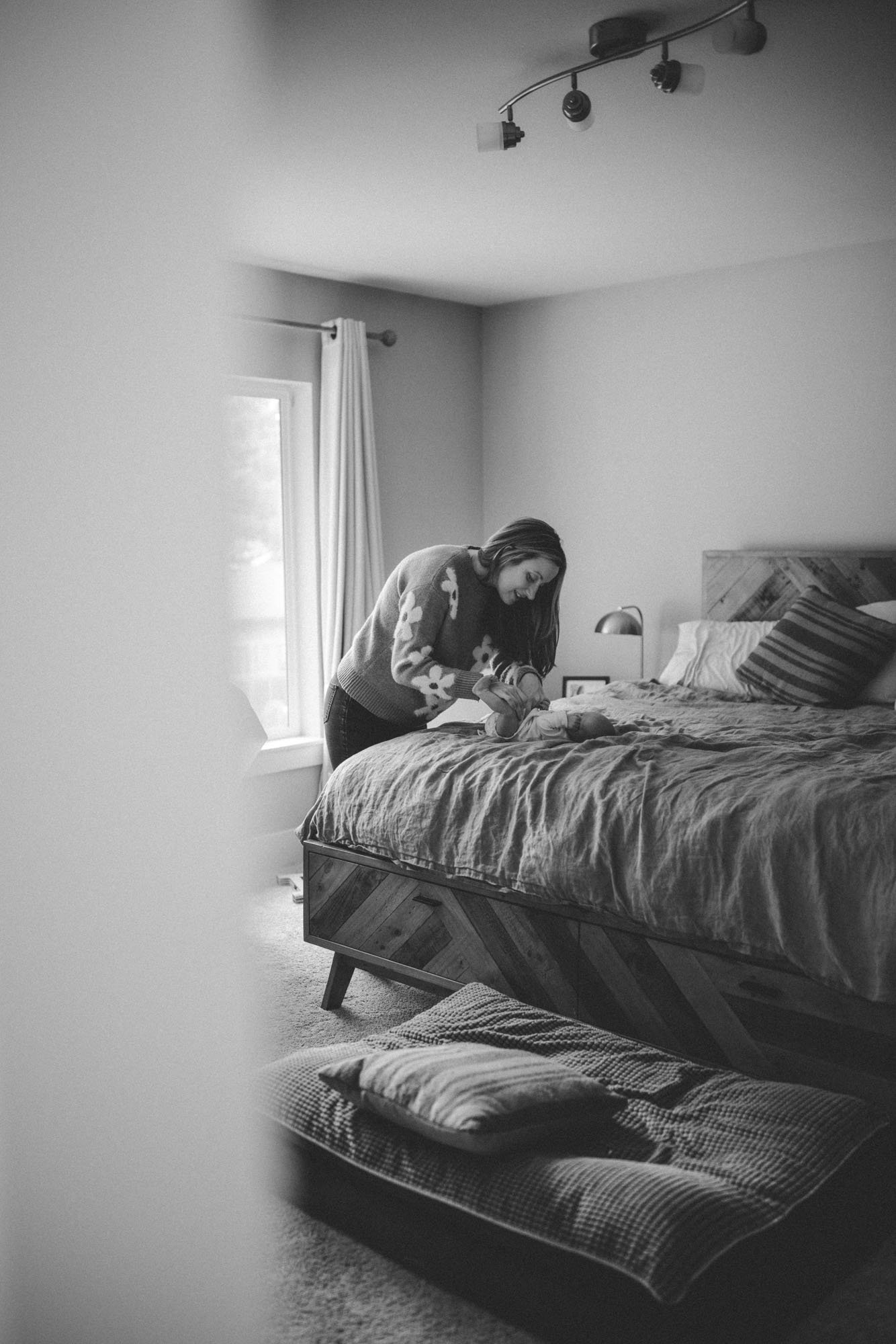 A mother gently changes her newborn on the bed during a calm in-home lifestyle newborn photography session in Seattle.
