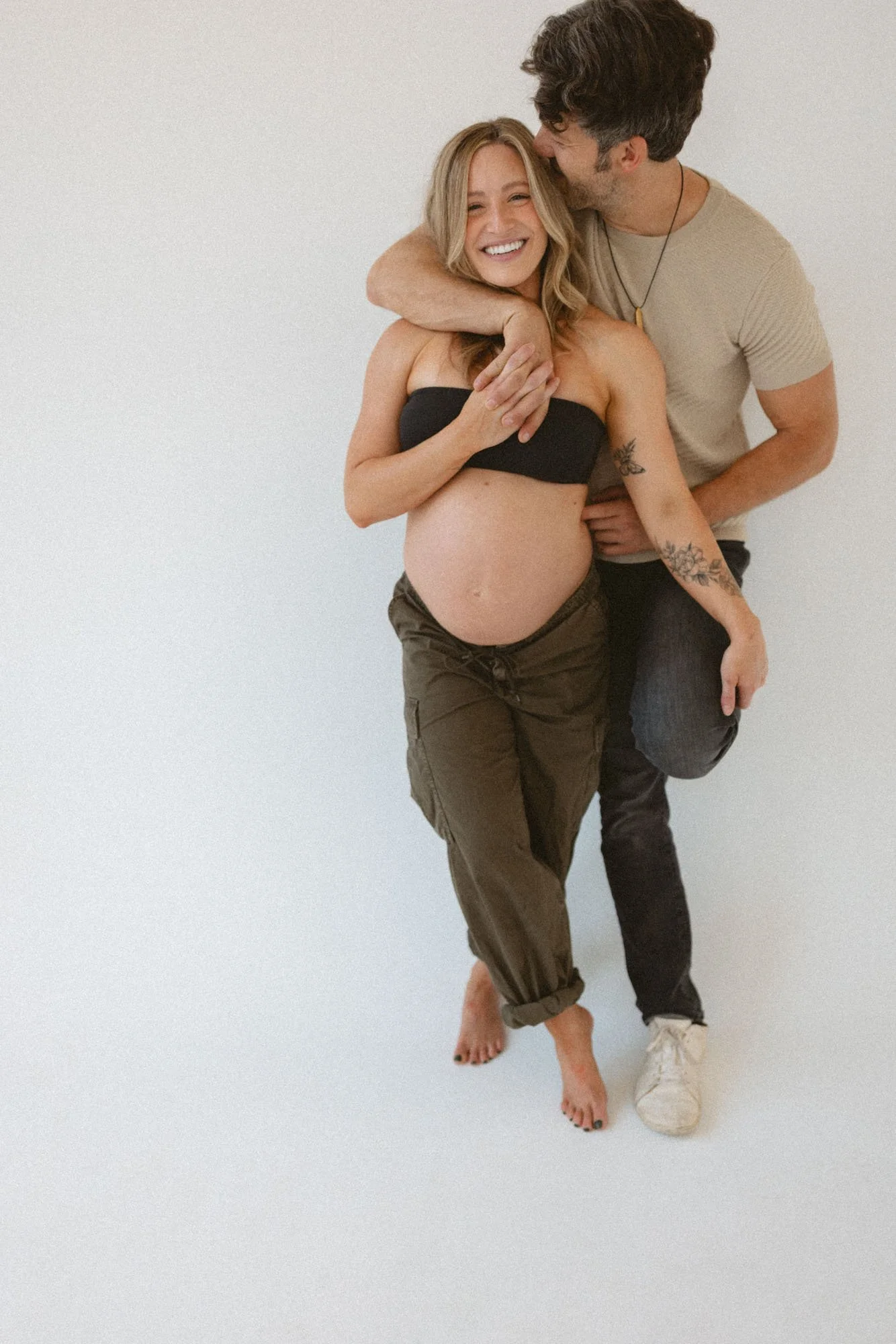 Pregnant woman laughing as her partner kisses her during a relaxed maternity photography session in a Seattle studio.
