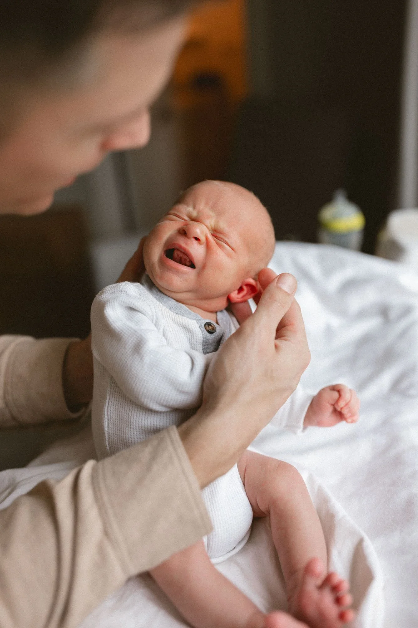 A newborn cries softly while being comforted in their father’s arms during a cozy in-home newborn photography session in Seattle.