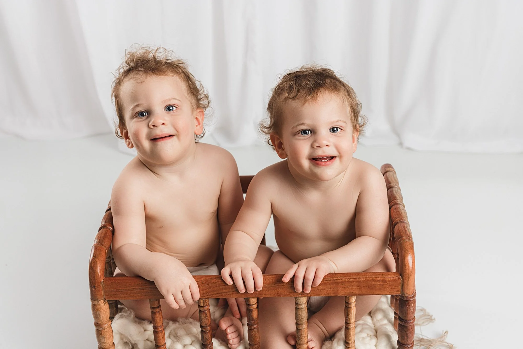 Twin babies sitting together in a wooden bench, looking toward the camera during a milestone photography session for a first birthday in Gig Harbor, Washington