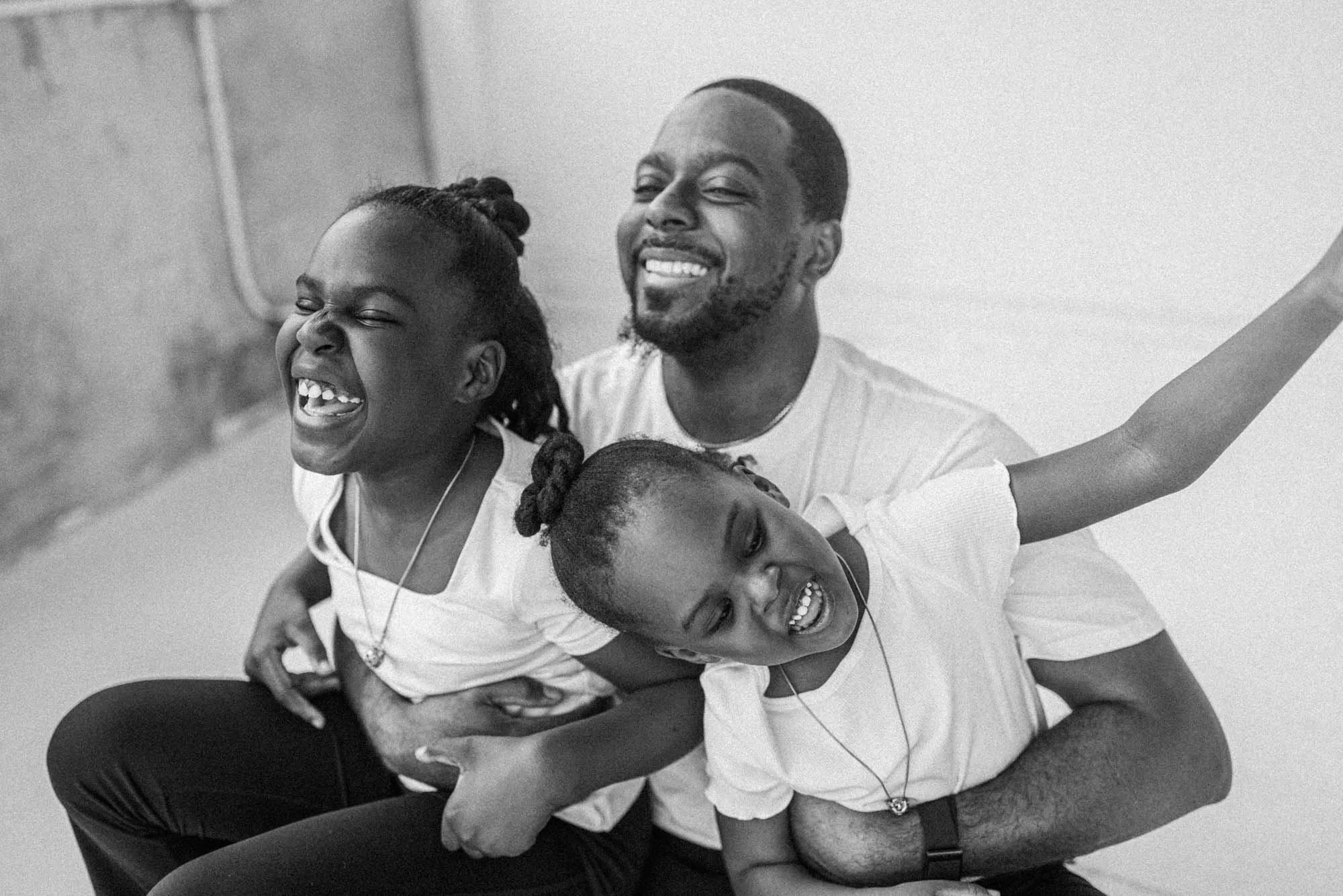 Father laughing with his daughters during a joyful studio family session, photographed by a Seattle family photographer. Black and white portrait highlighting connection, emotion, and genuine family interaction.