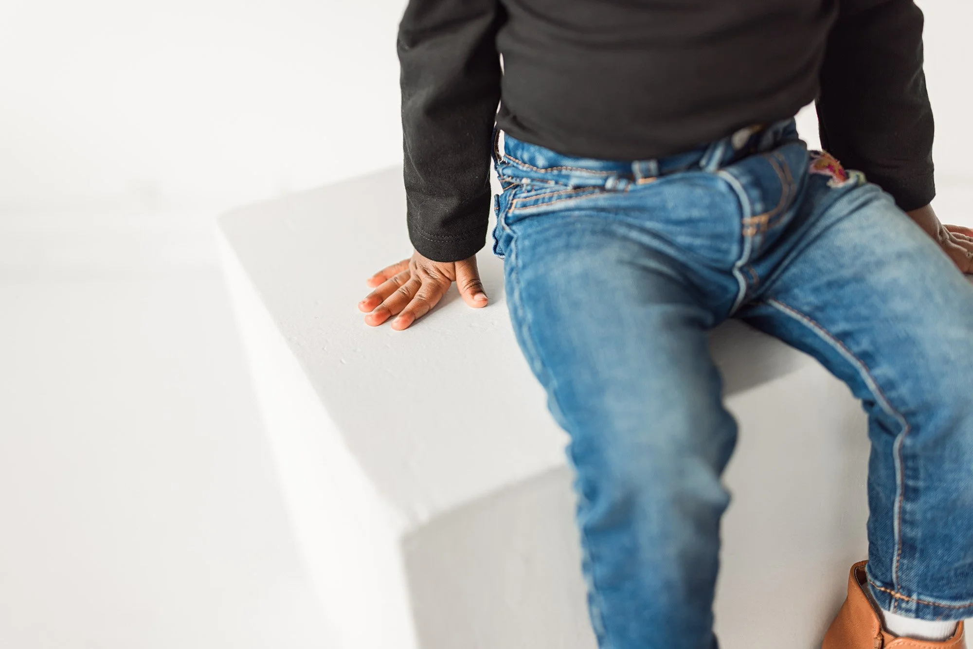 Close-up detail of baby hands and denim outfit during a studio milestone session, photographed by a Seattle baby photographer. Minimal, clean composition highlighting texture, movement, and timeless baby photography style.