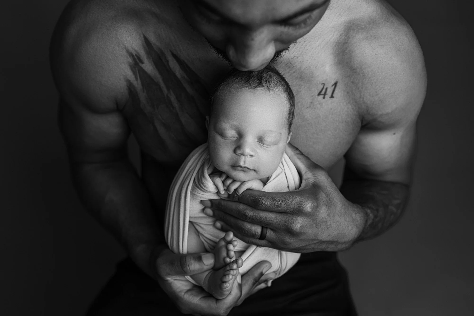 Black-and-white portrait of a father holding his sleeping newborn baby against his chest