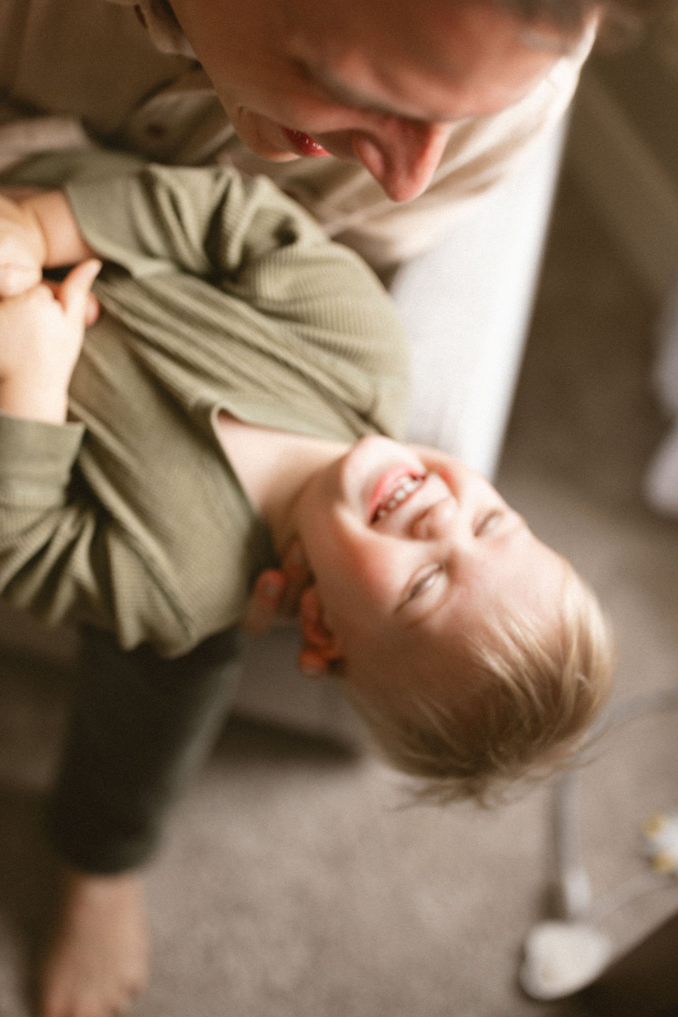 A toddler laughs while being playfully held upside down by a parent during a cozy in-home lifestyle family photography session in Seattle.