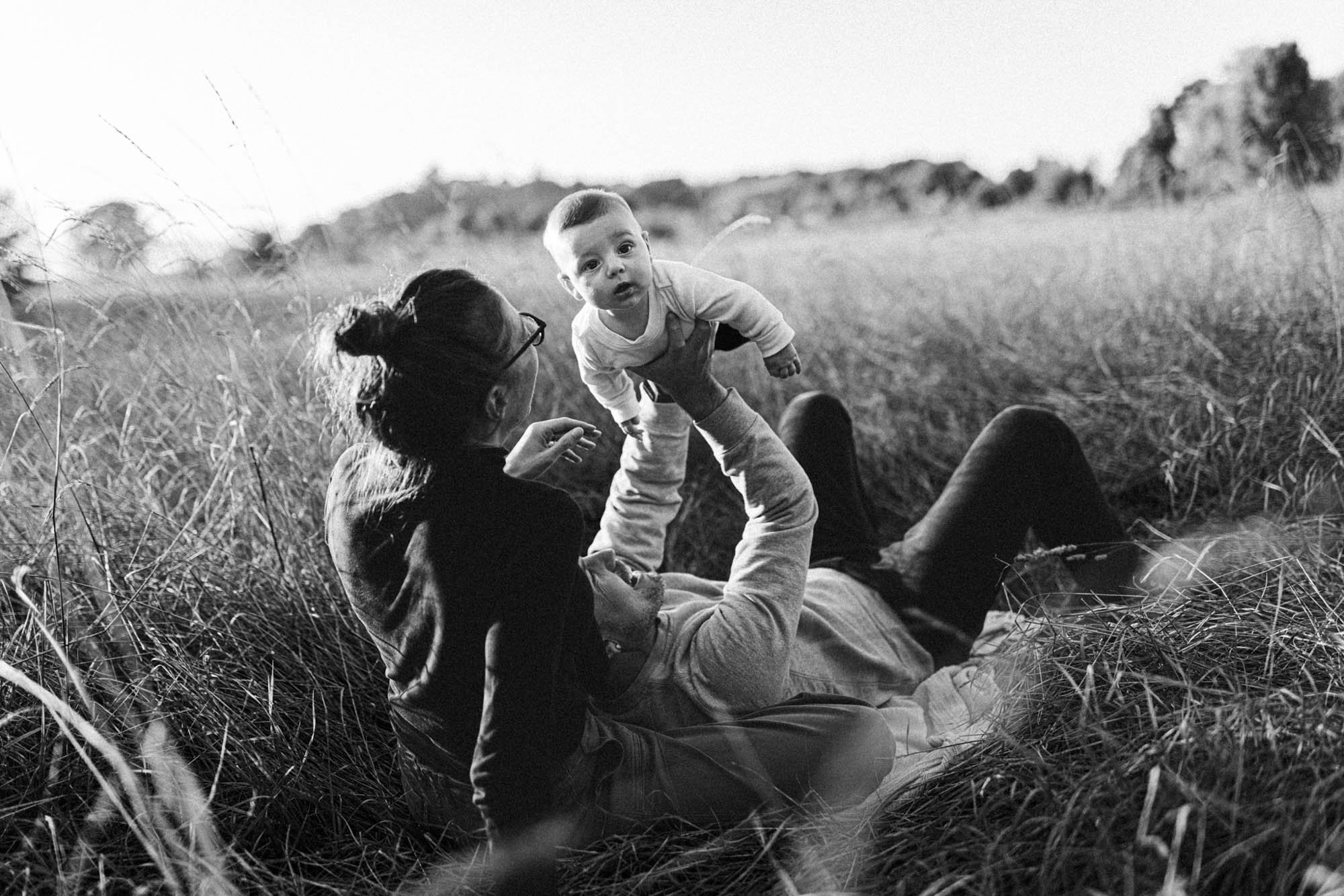 Mother and father lying in a grassy field lifting their baby in the air during a natural outdoor family photography session in Seattle.
