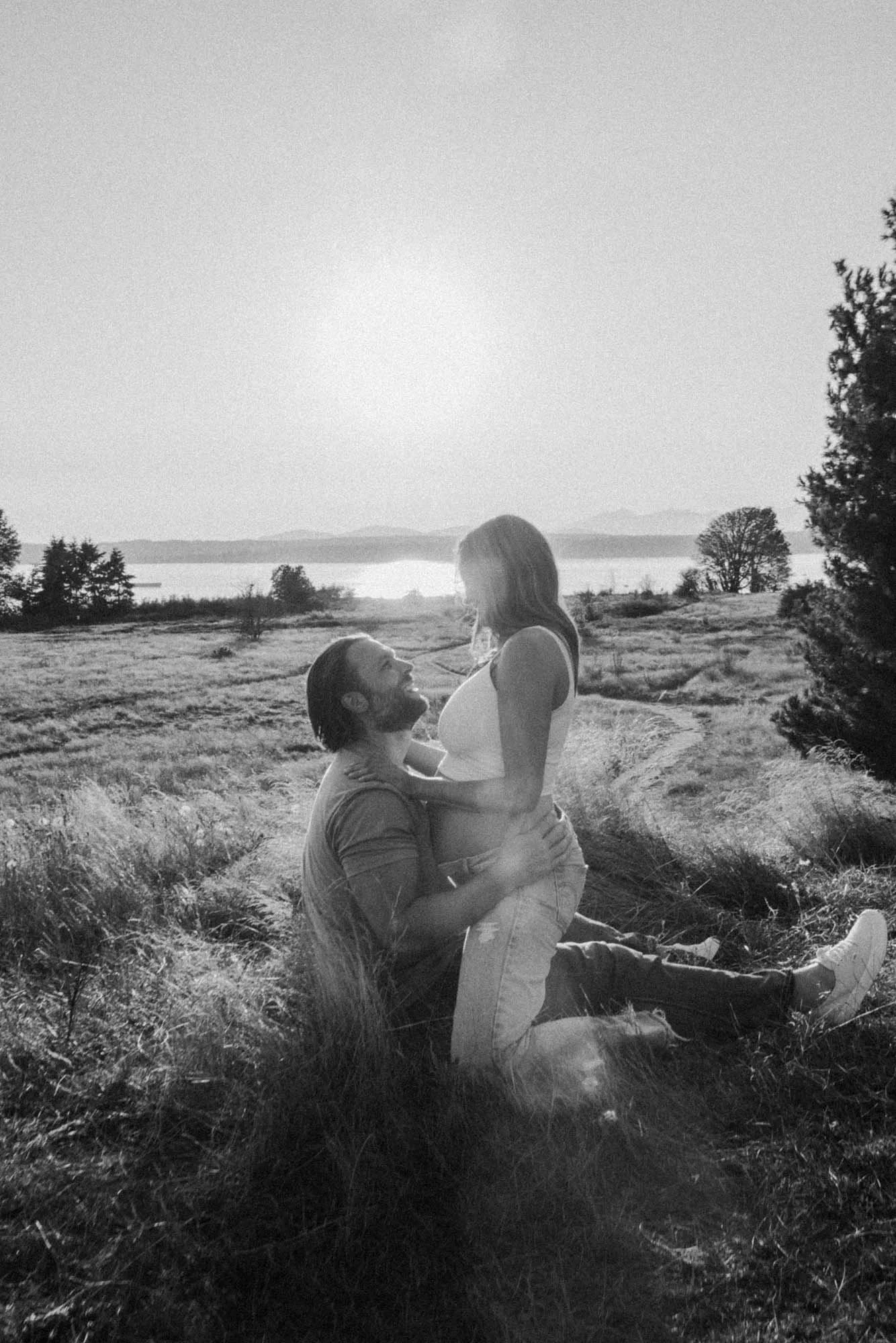Couple embracing during a maternity session in an open field, capturing a quiet and intimate moment in black and white in Discovery Park