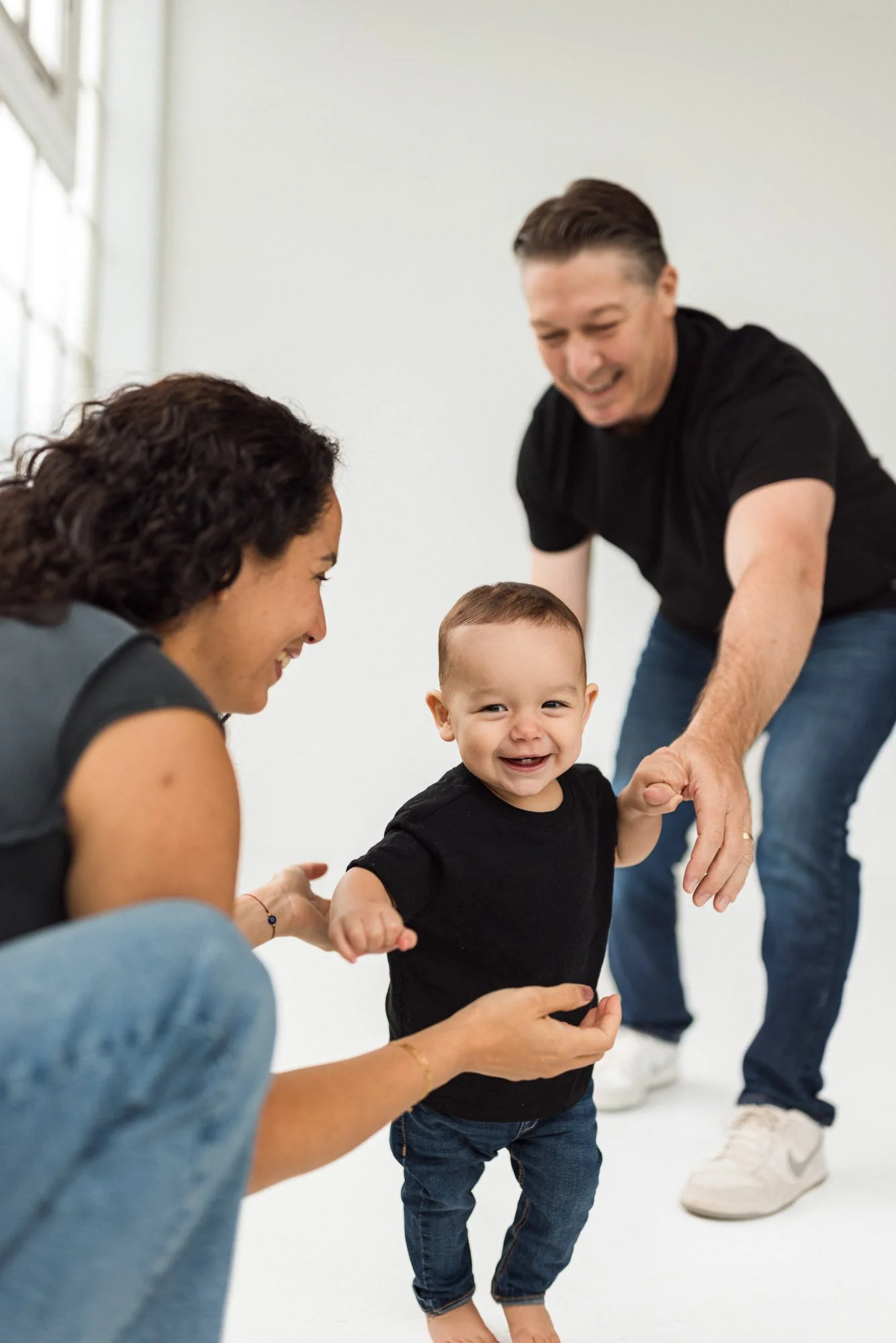 Baby taking first steps with support from parents during a studio family session, photographed by a Seattle family photographer. Joyful, candid moment highlighting connection, movement, and milestone development in a clean, modern studio environment.