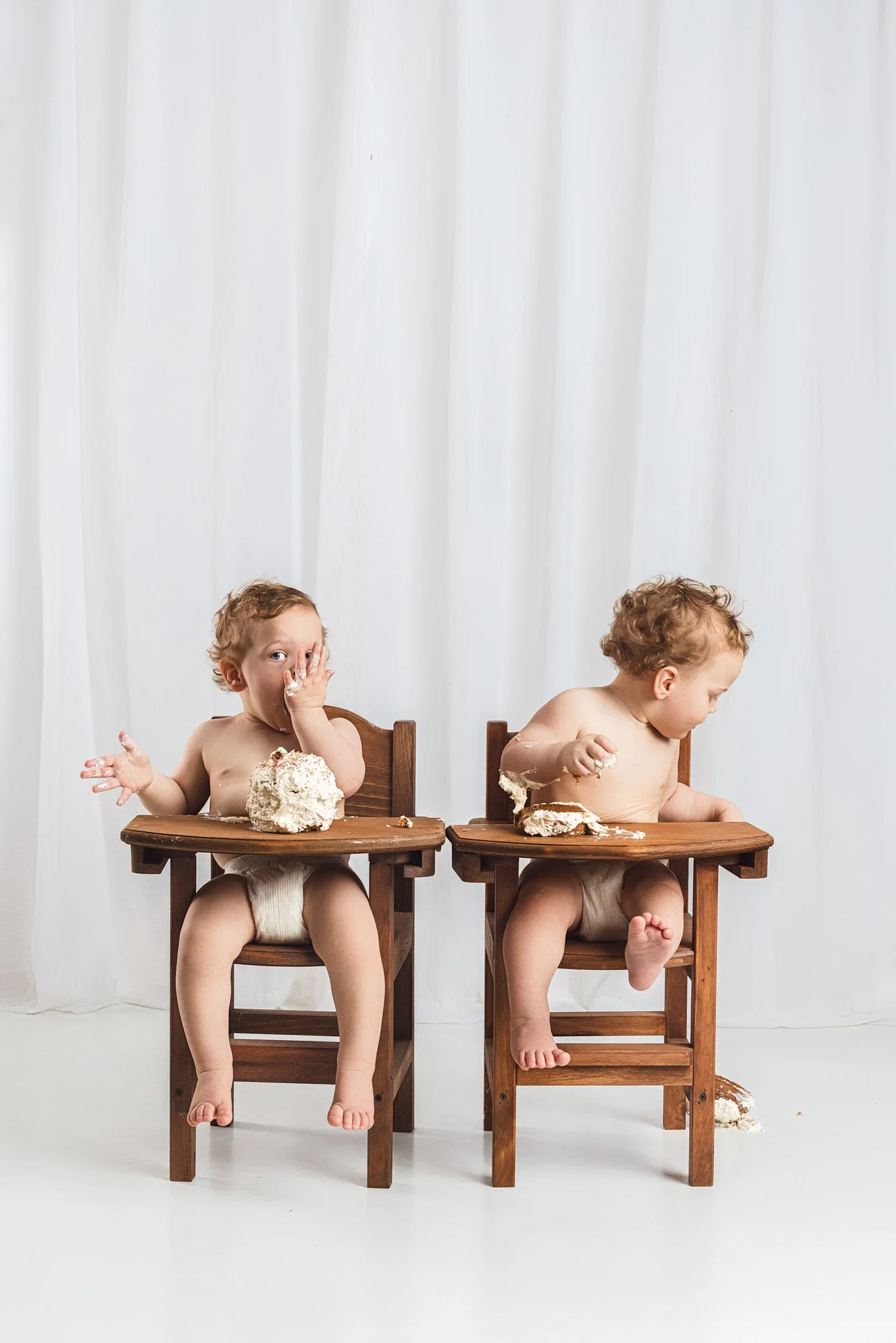 Twin babies reacting differently to cake during a first birthday cake smash session in a Seattle photography studio
