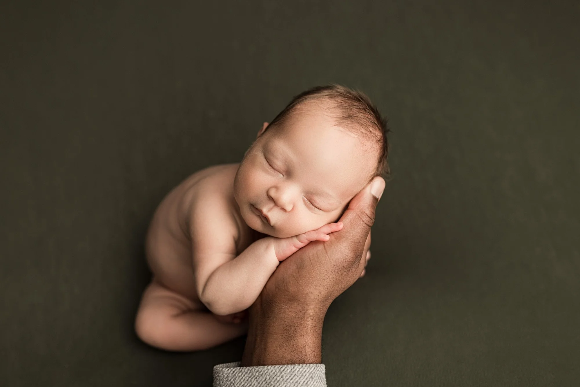 Sleeping newborn baby gently supported by a parent’s hand during a studio portrait