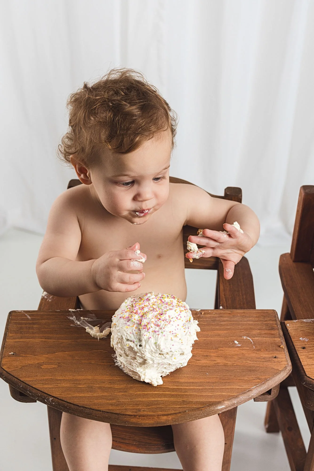 Baby enjoying a first birthday cake smash session in a minimalist studio setup near Bellevue, Washington, photographed by Seattle milestone photographer Atsumi Sullivan Photography.
