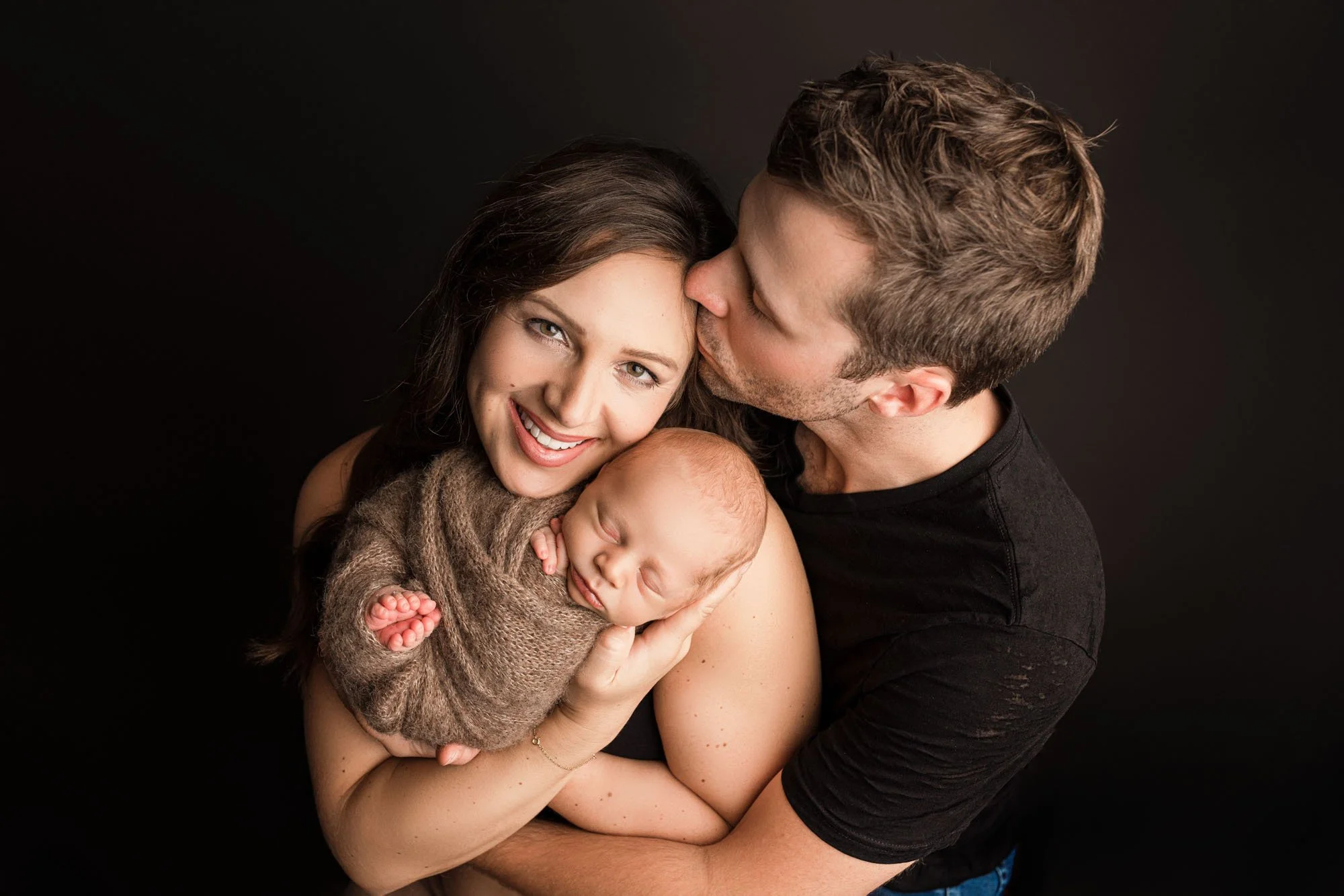 Parents holding their newborn baby during a studio session, with dad kissing mom’s forehead — intimate, connection-focused newborn family photography in Seattle