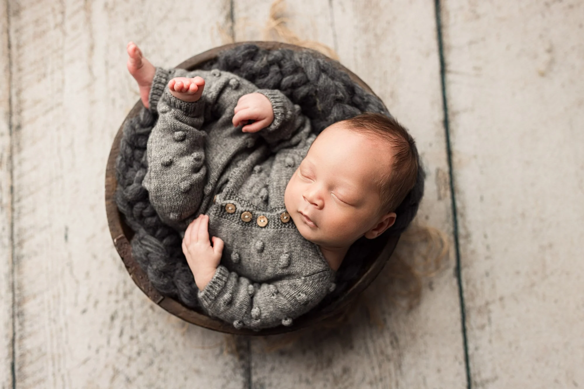Newborn baby sleeping in a round basket while wearing a soft gray knitted outfit