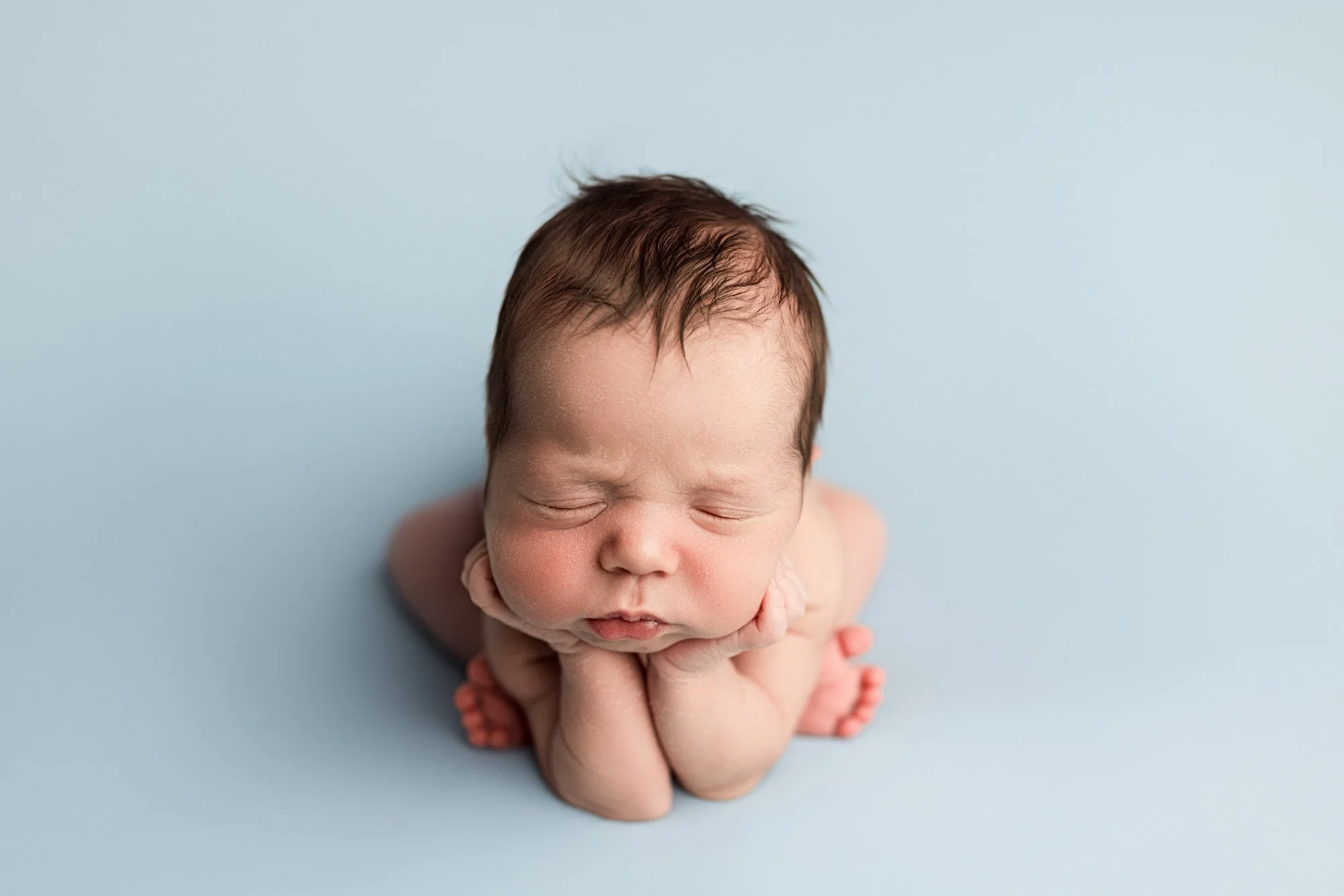 Sleepy newborn baby posed in froggy pose on a soft blue backdrop during a studio newborn photography session in Seattle by Atsumi Sullivan Photography.