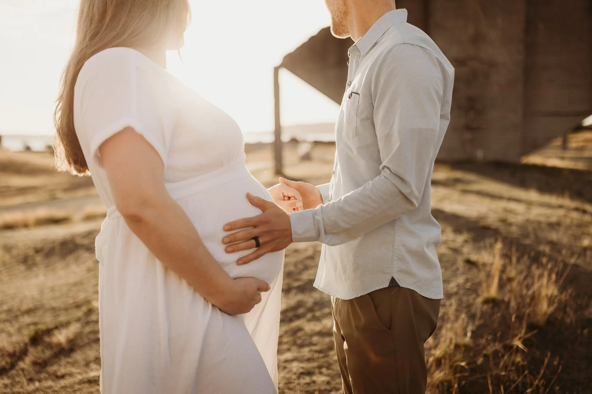 Close-up of expecting parents holding baby bump in warm golden light during an outdoor maternity session in Seattle