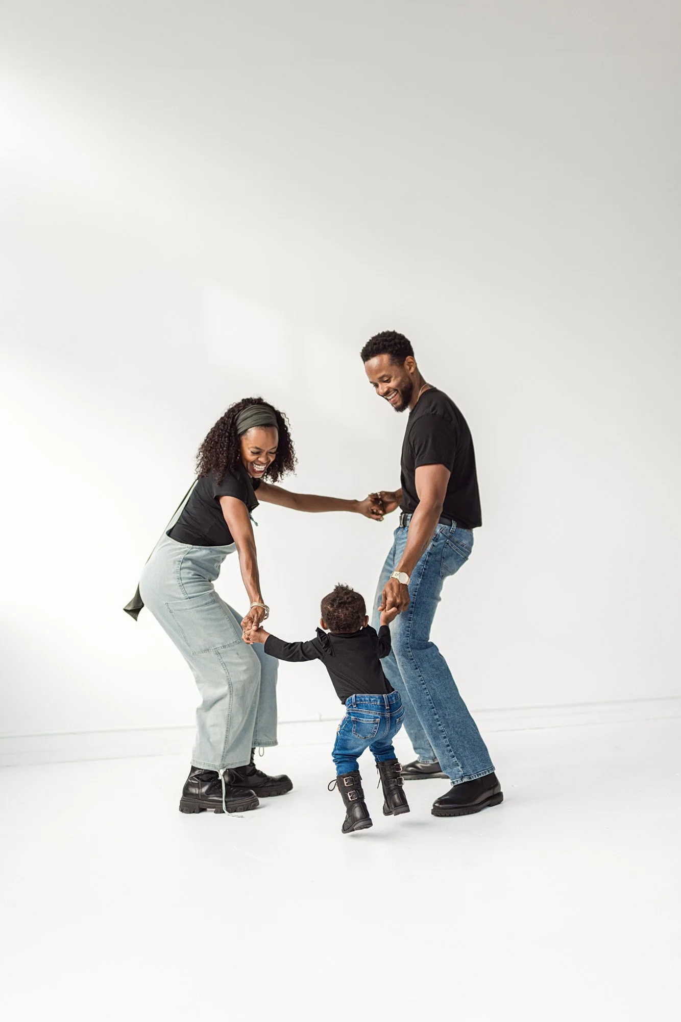 Parents holding hands with their toddler and playing together during a joyful Seattle natural light studio family photography session.