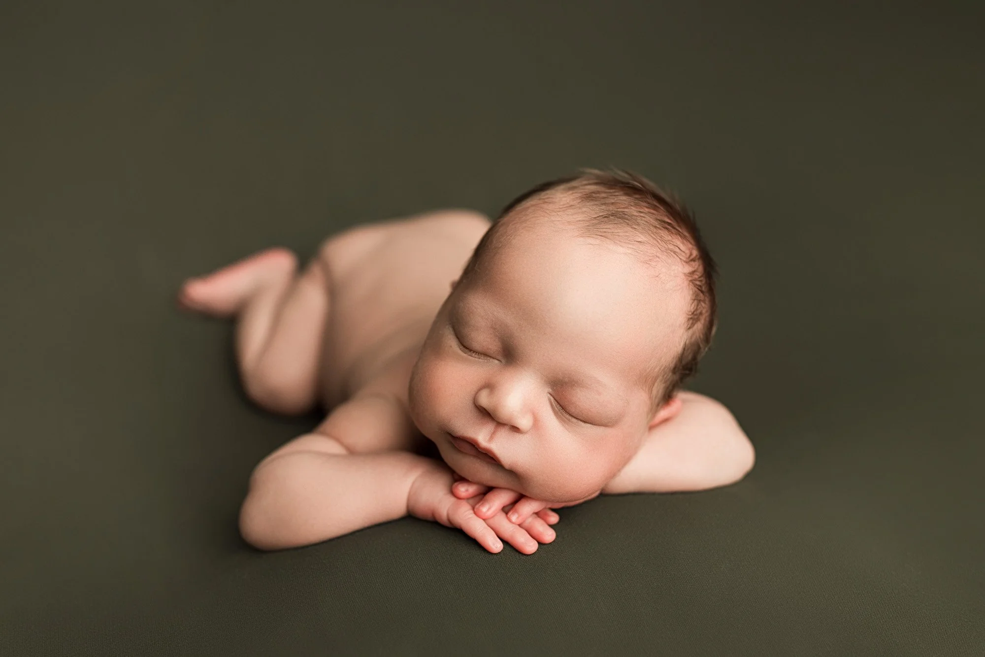 Twenty-five-day-old newborn baby sleeping with hands folded beneath the chin