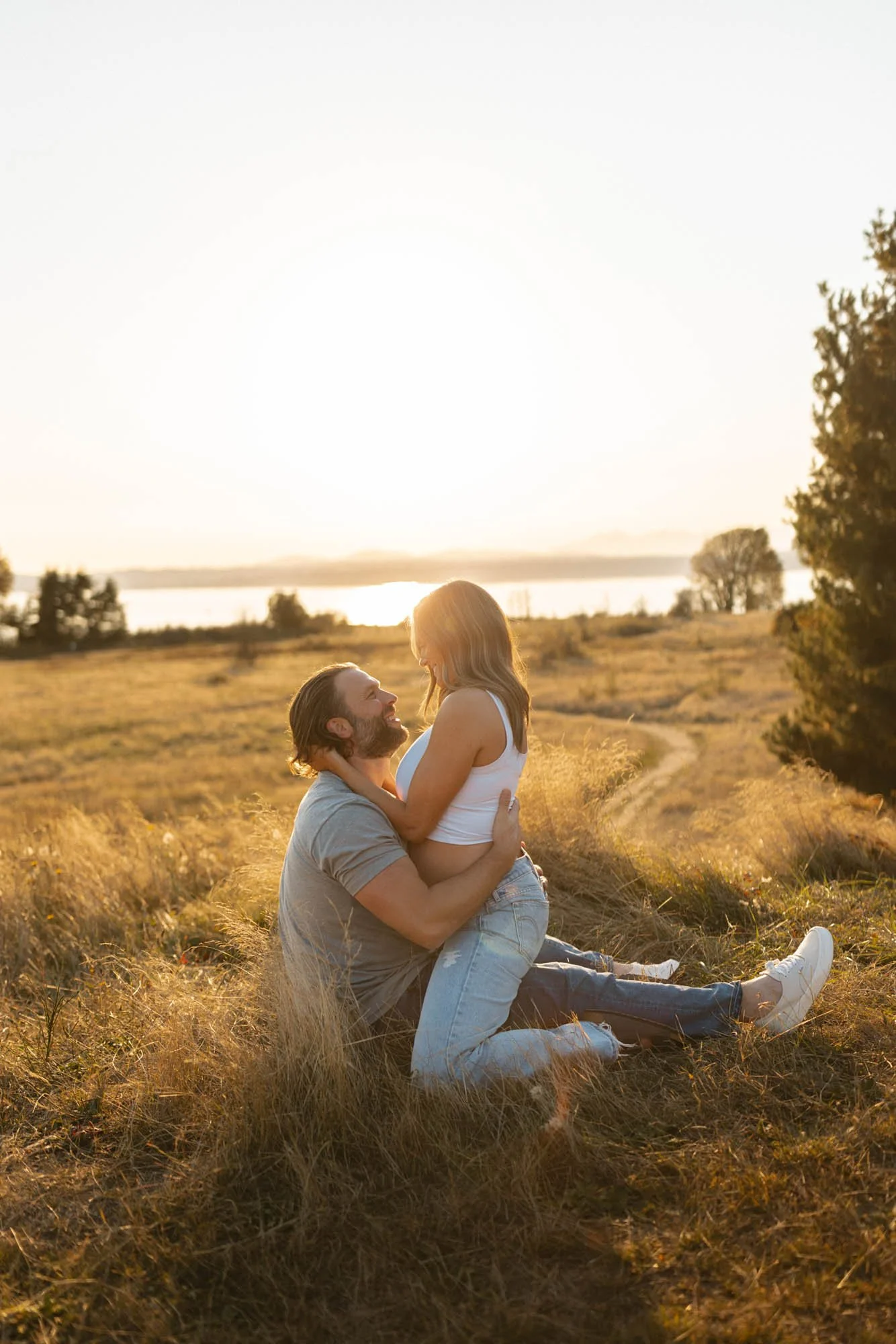 Expecting couple embracing during a golden hour maternity photography session at Discovery Park in Seattle.