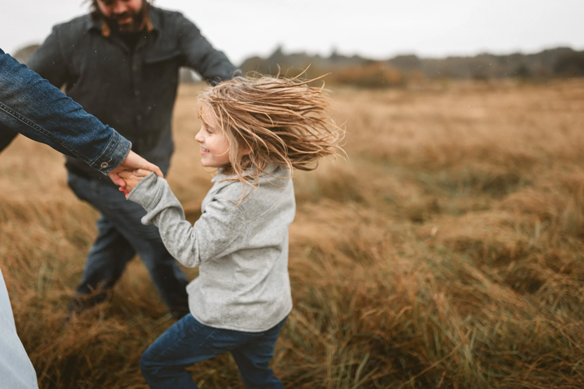Child running and holding hands with parents in an open field during a natural outdoor family photography session in Seattle.