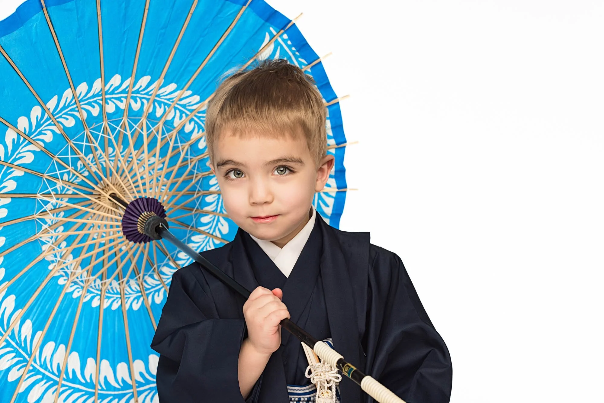 Little boy in navy kimono holding a blue Japanese umbrella, studio portrait on clean white background – Seattle kimono photography, Shichi-Go-San style child portrait