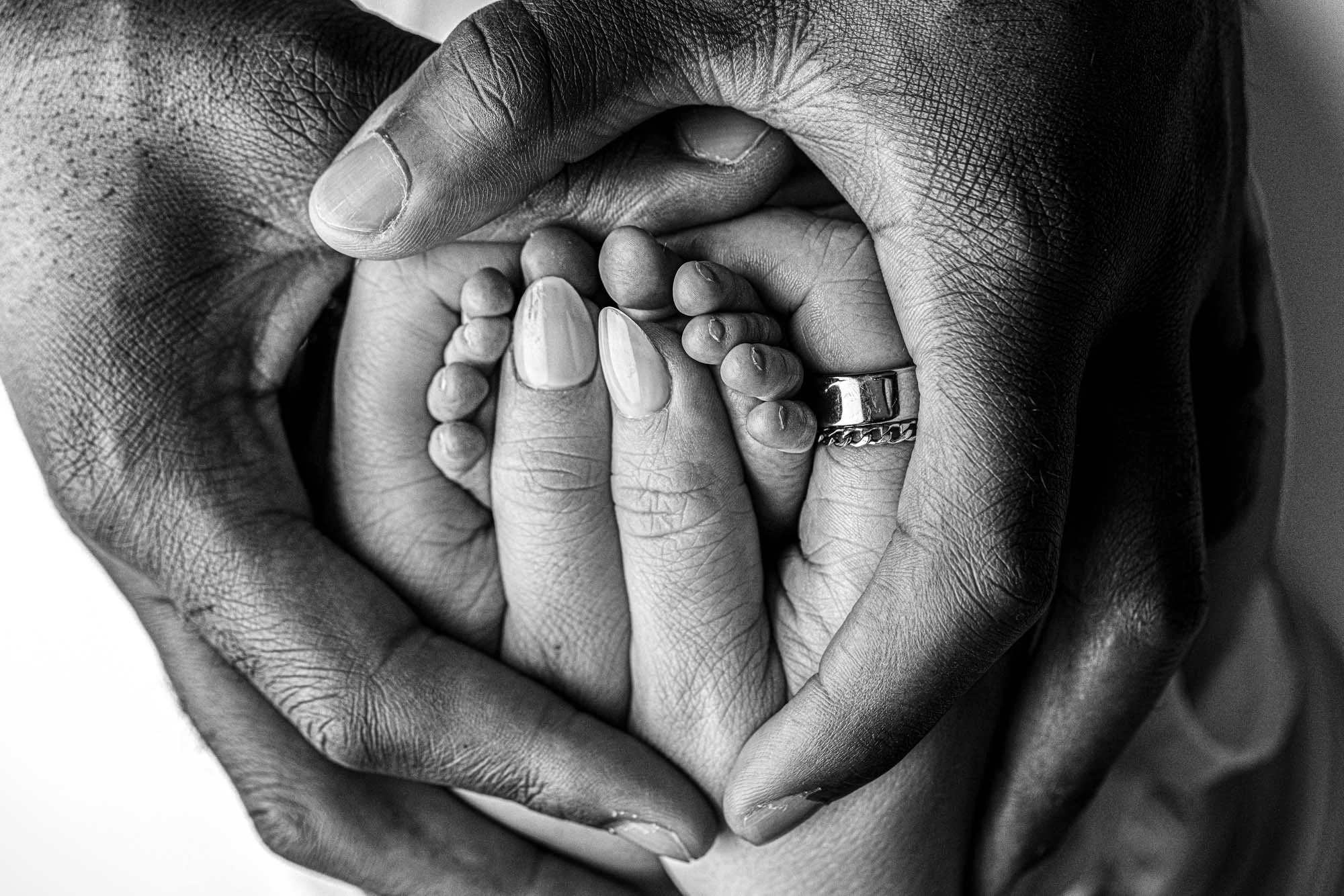 Close-up of a newborn baby’s tiny feet cradled in both parents’ hands