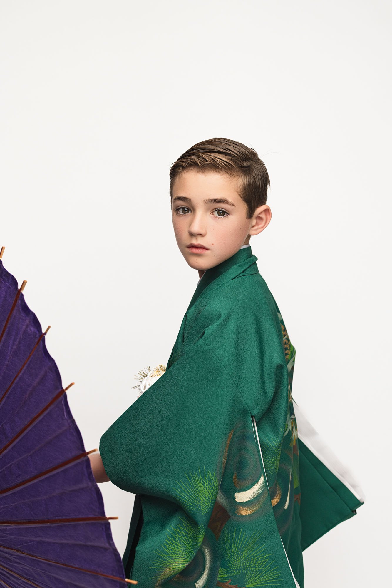Young boy in green traditional kimono holding a purple umbrella during a Shichigosan portrait session in a Seattle studio