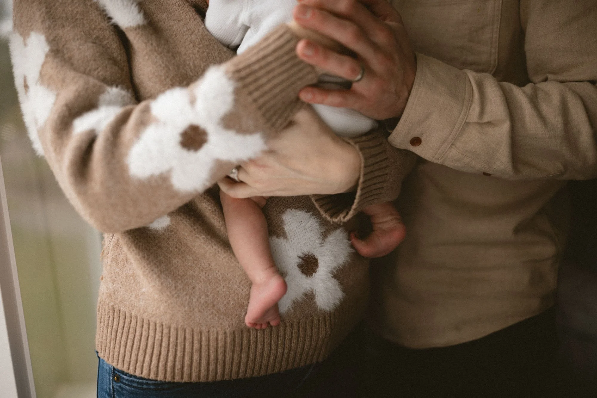 Close-up of a newborn’s tiny feet resting in their parents’ hands during a cozy in-home newborn photography session in Seattle.