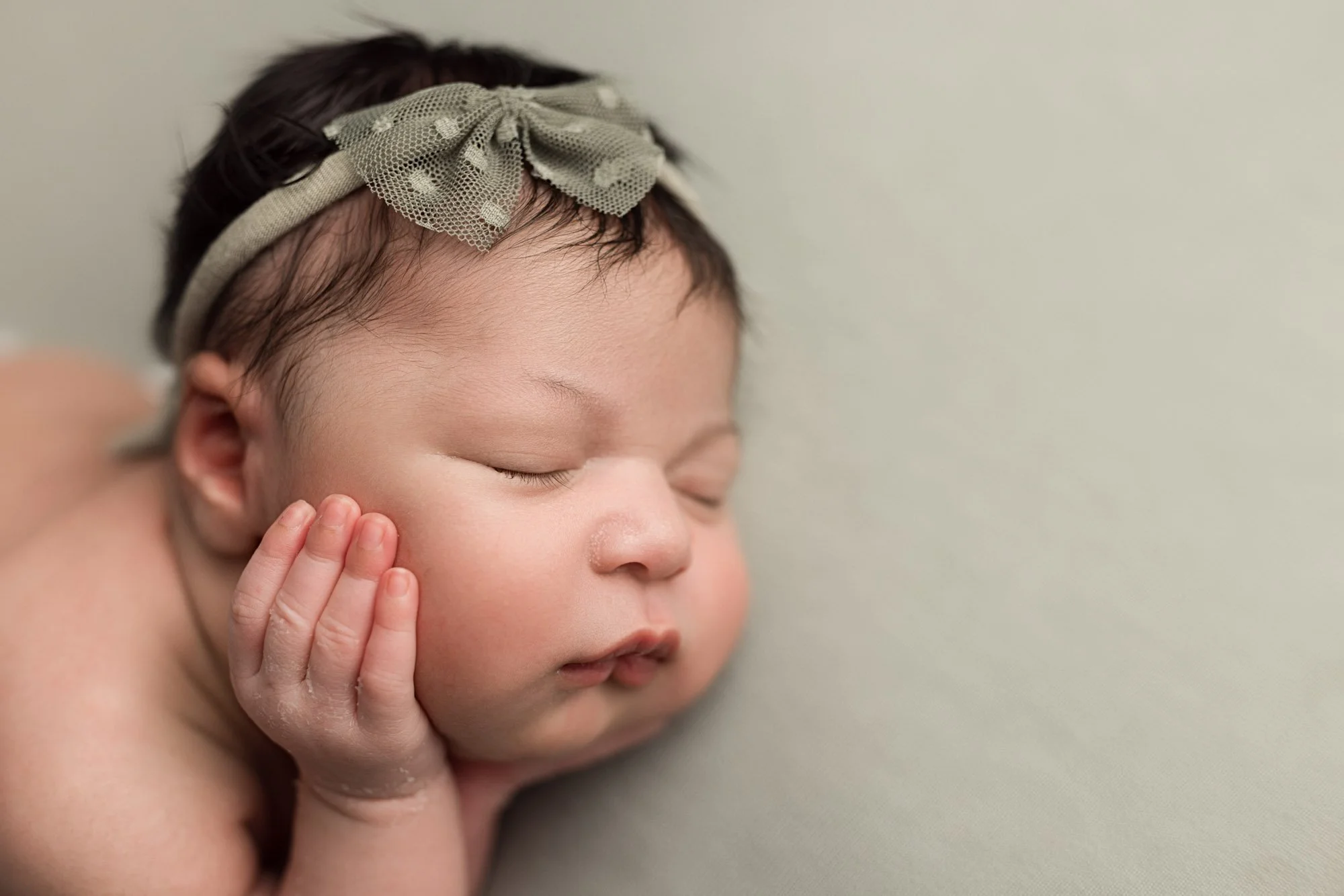 Close-up of a sleeping newborn baby girl wearing a delicate bow during a Seattle studio session