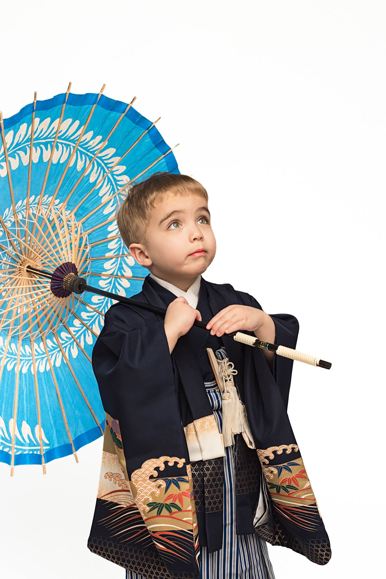 Young boy in traditional Japanese kimono looking up while holding wagasa umbrella, minimalist studio portrait – Seattle children kimono session