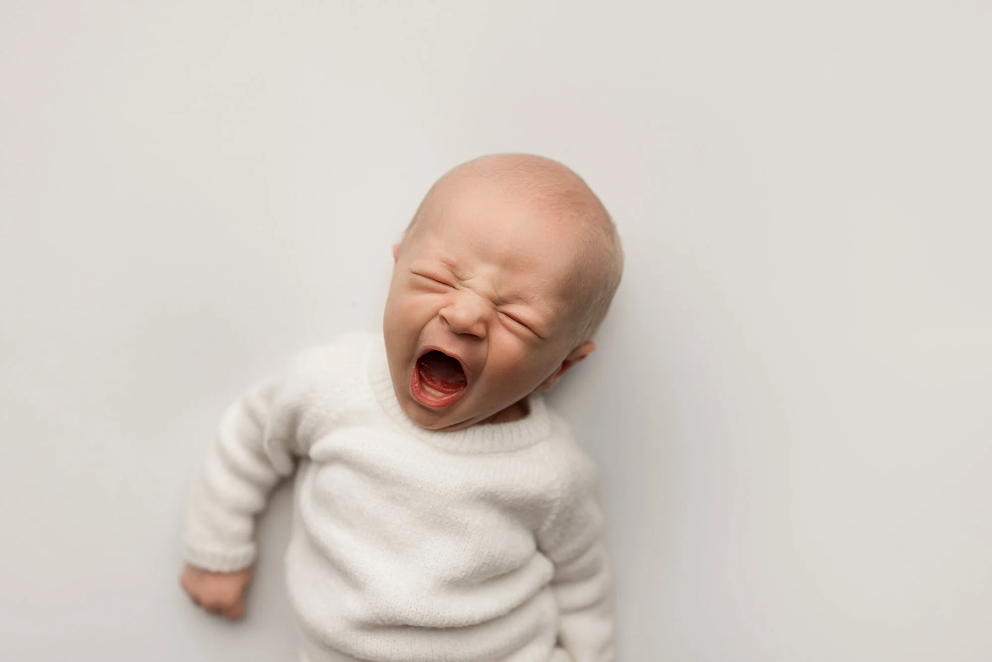 Newborn baby wearing a soft white outfit and yawning during a Seattle studio photography session.