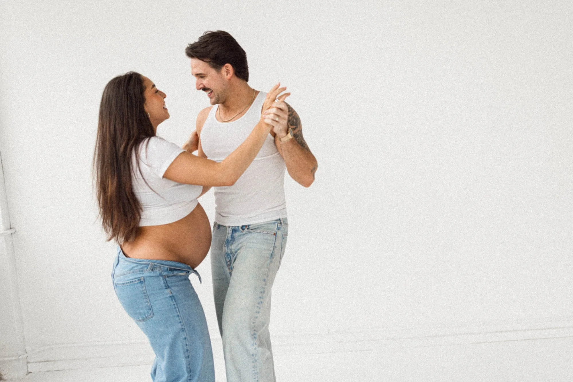 Expecting parents sharing a joyful moment together during a relaxed natural light maternity session in a Seattle studio.