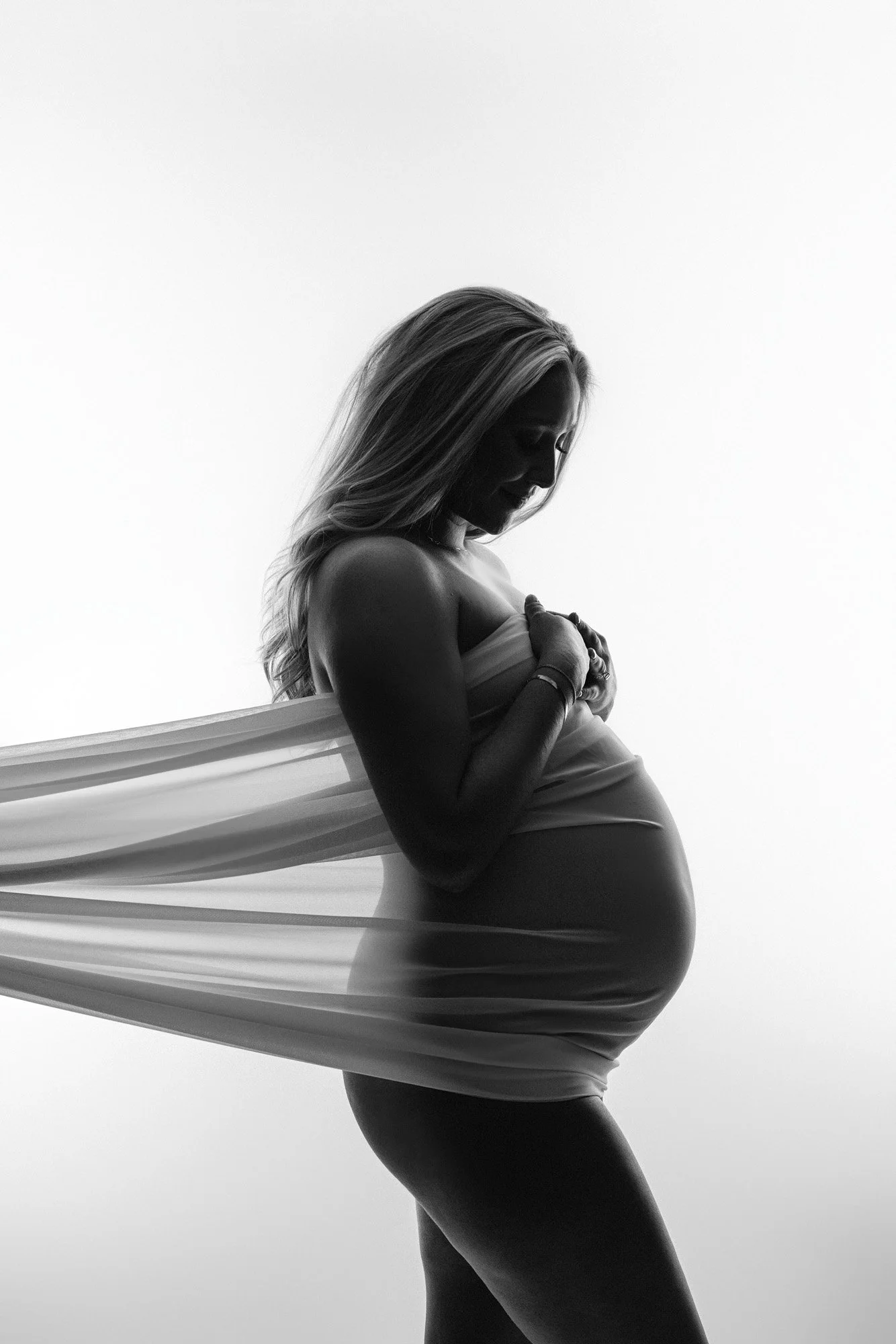 Fine art black and white maternity portrait of an expecting mother holding her baby bump with flowing fabric during a studio maternity photography session near Seattle.