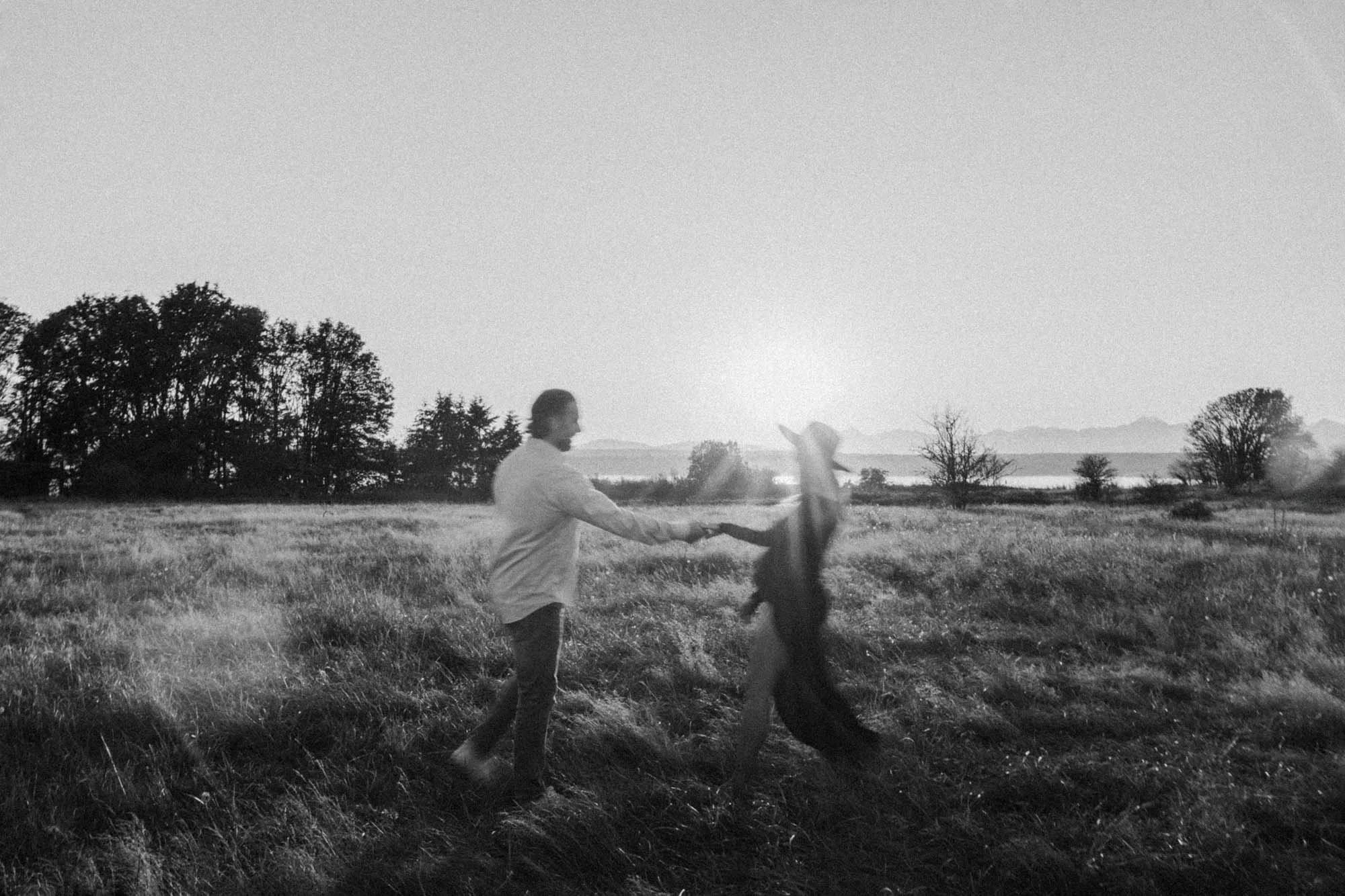 Couple spinning together in a field during a maternity session, capturing movement and connection in a black and white photograph
