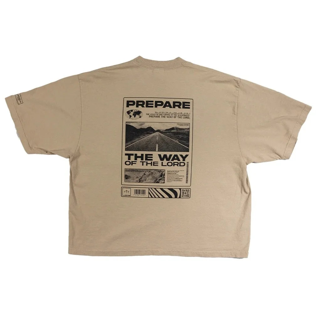 Beige T-shirt with black graphic print on the back, featuring a road leading into mountains, titled 'PREPARE THE WAY OF THE LORD.'