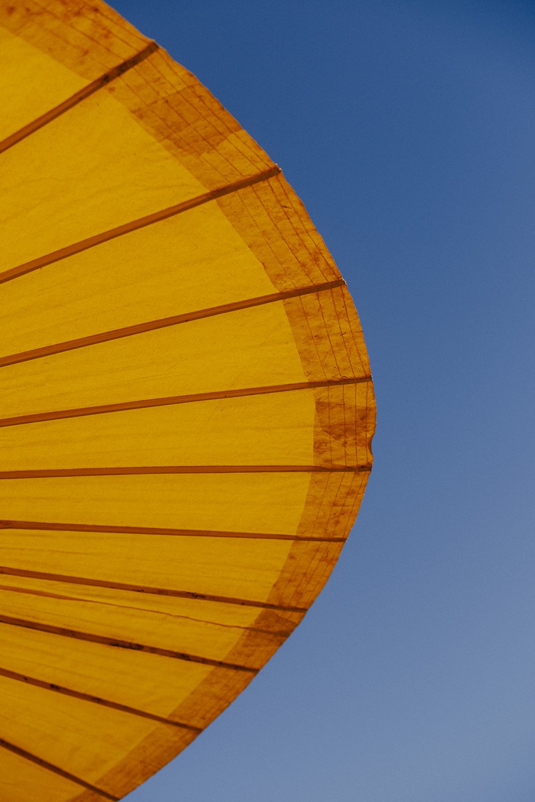 Part of a yellow beach umbrella against a blue sky.