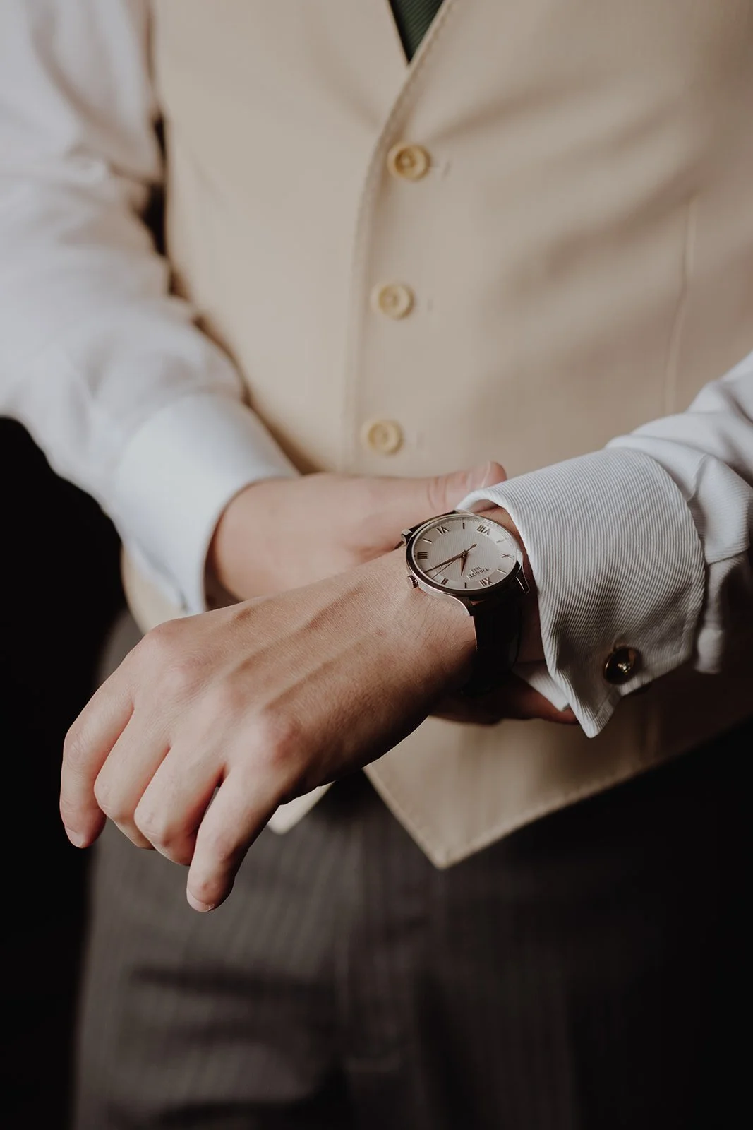A person wearing a white dress shirt with a beige vest and a watch on their wrist.