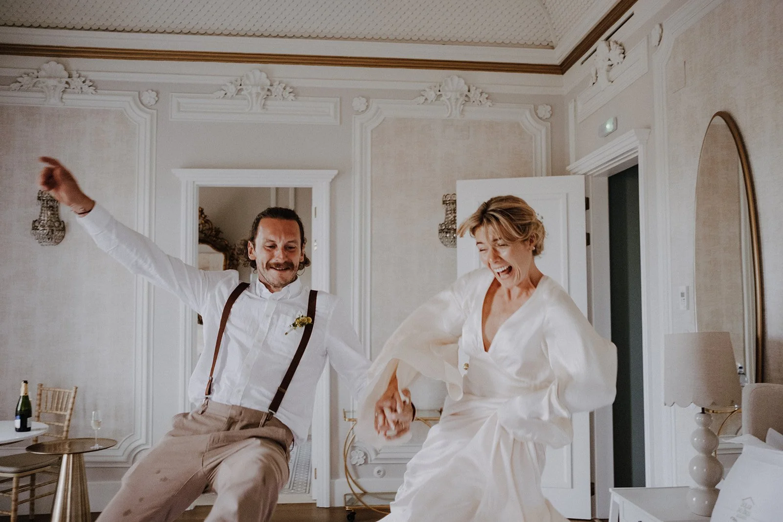 A man and woman dancing joyfully in a well-decorated room, holding hands and smiling.