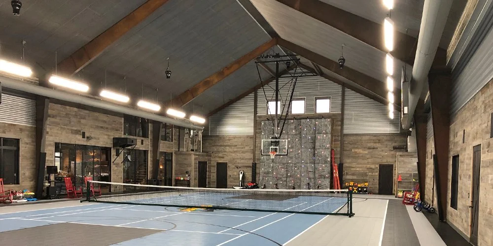 Indoor sports facility with a basketball hoop, a volleyball net, and a rock climbing wall on the back wall.