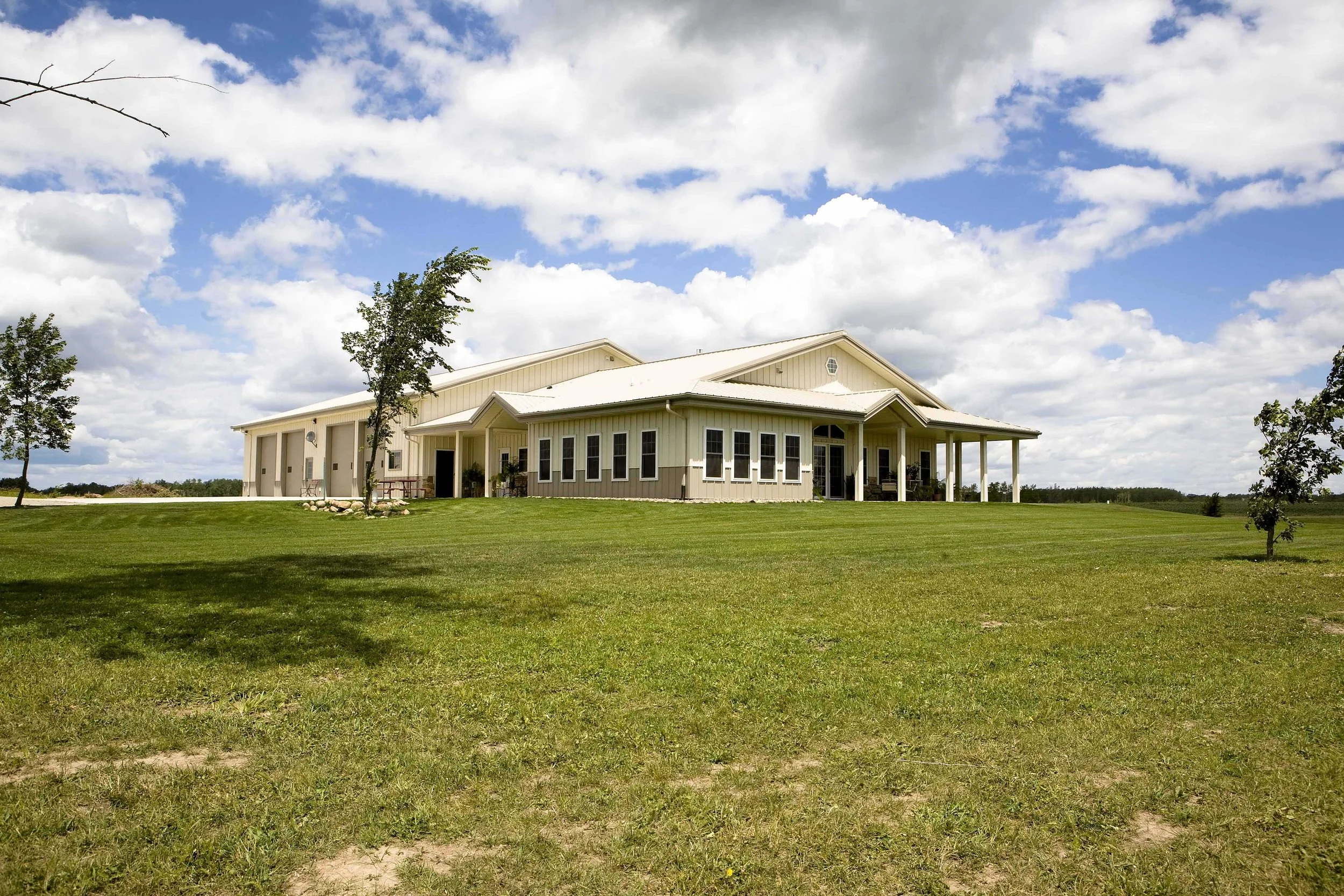 Large beige house with a covered porch on a vast grassy lawn under a partly cloudy sky.