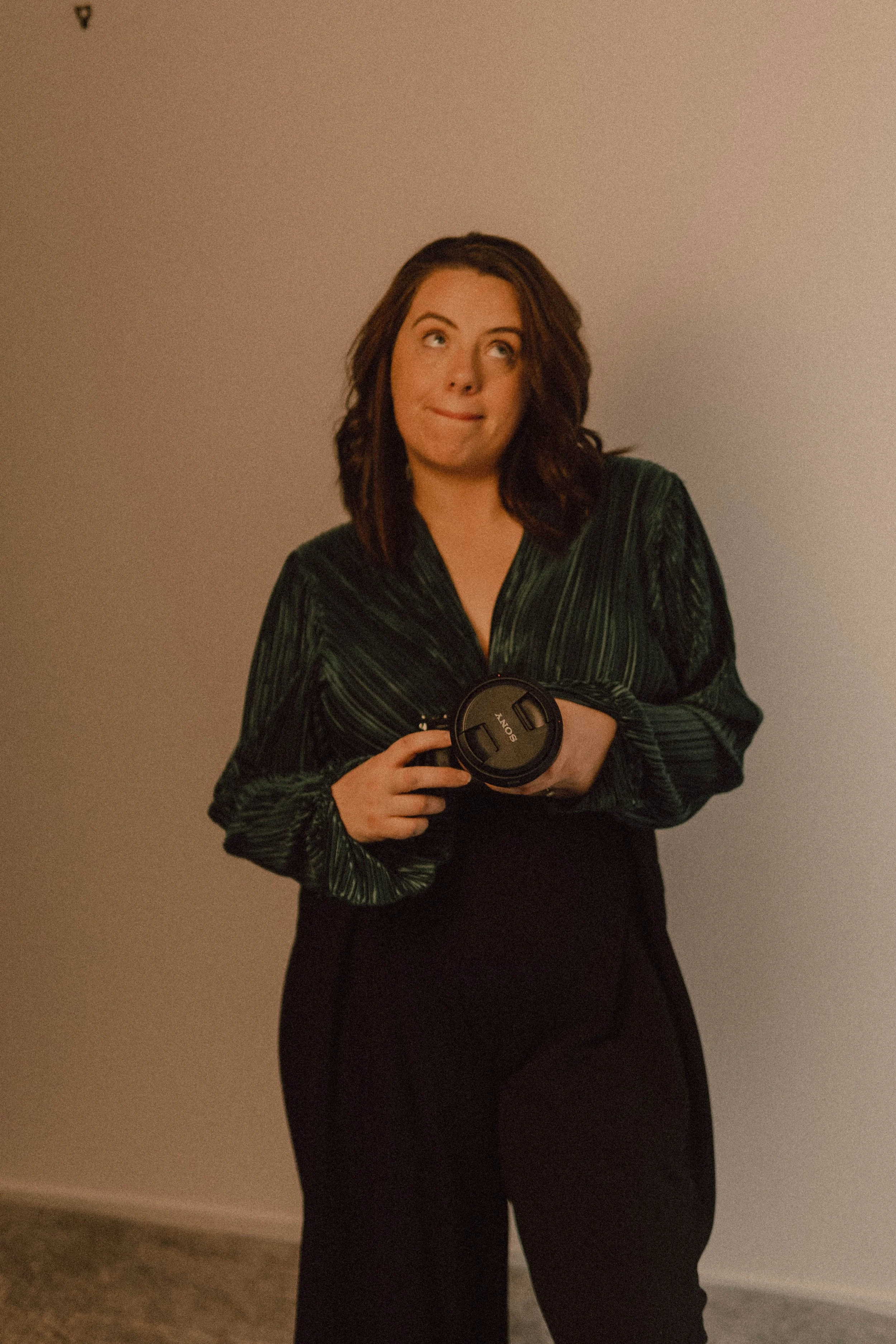 A woman with brown hair dressed in black pants and a dark green,  holding a camera. sassy branding photos